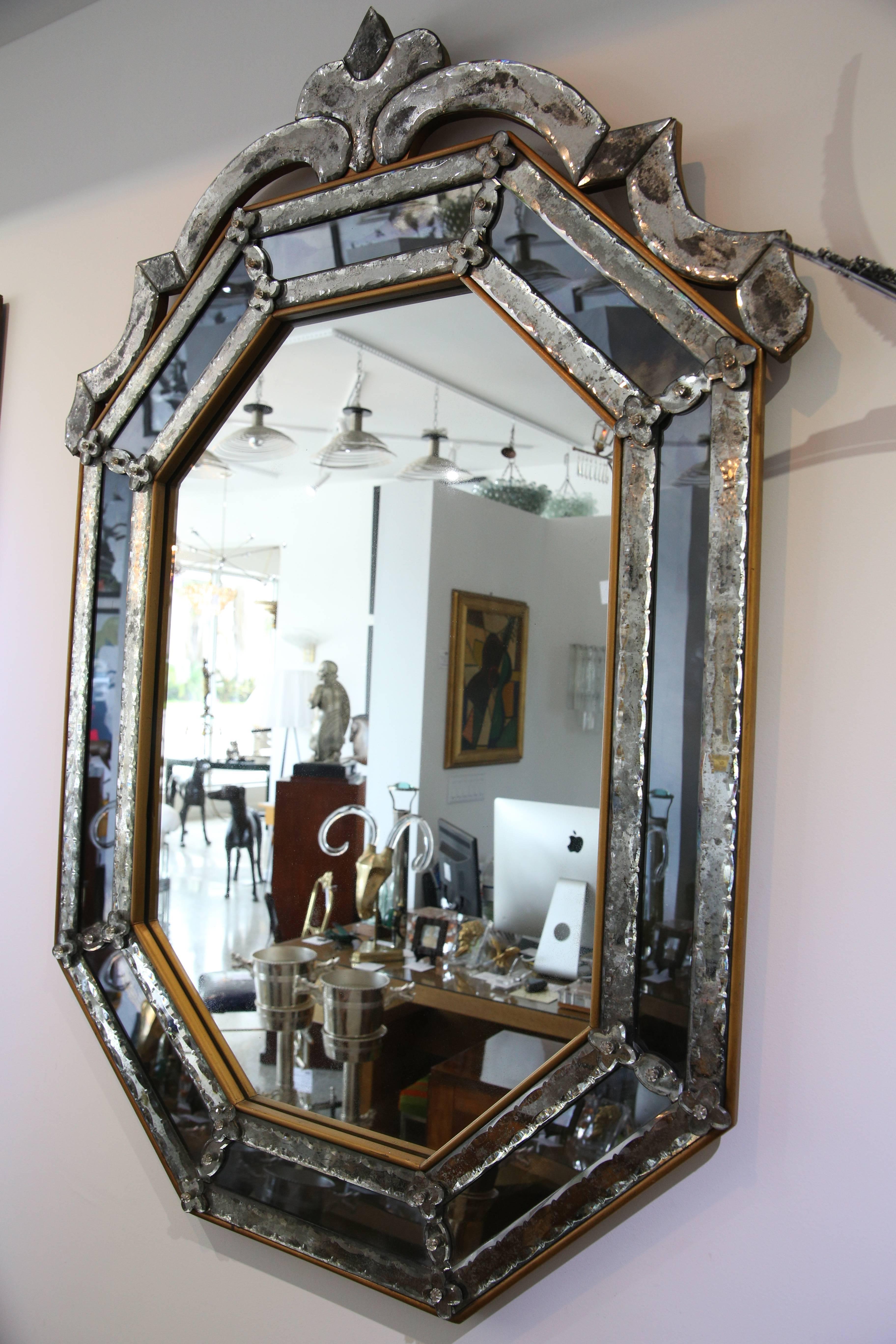 This stylish Venetian Murano glass mirror dates to the 1950s-1960s and is fabricated with antiqued, clear and smoked mirror. The wood frame has an antique gold coloration which frames the panels for a subtle contrast.