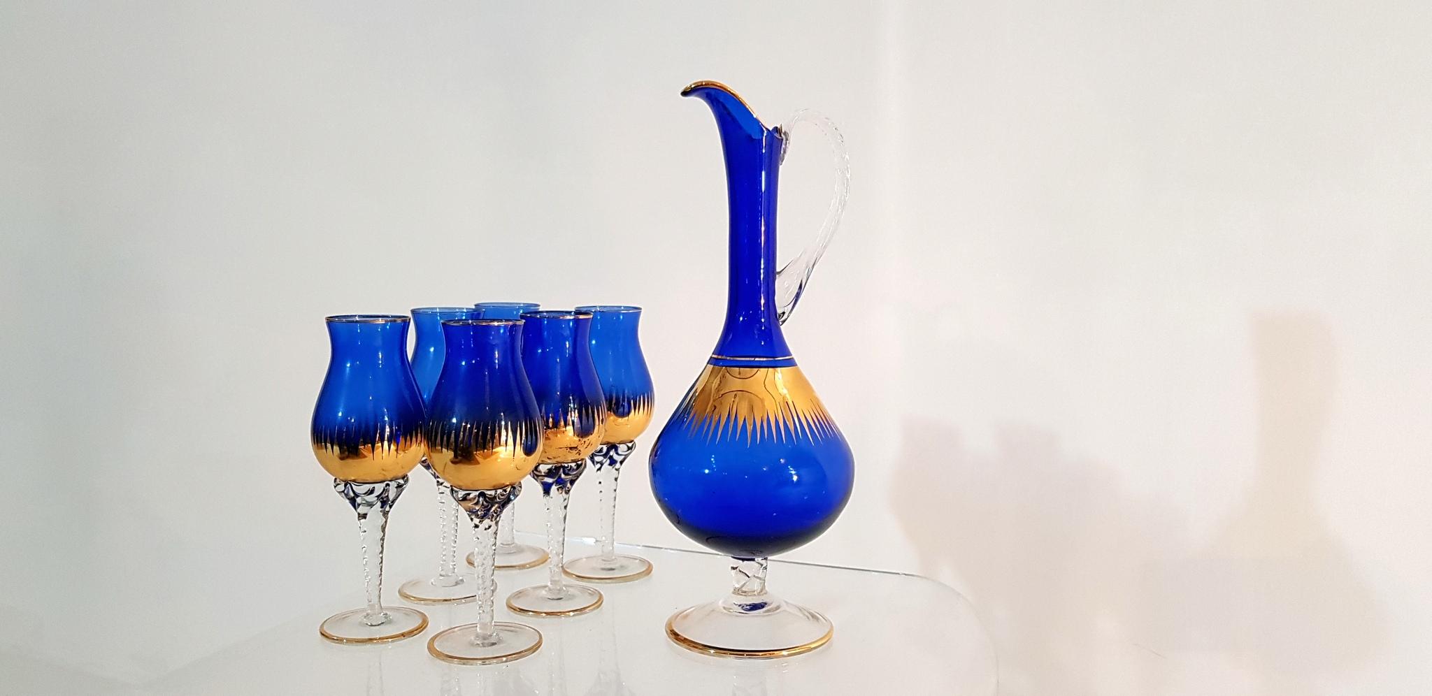 Set of six glasses and pitcher produced in Venice Italy during the 1950s. Made from cobalt blue glass and decorated with 24-carat gold. The glasses and pitcher have stems and handle in twisted clear glass contrasting against the blue and