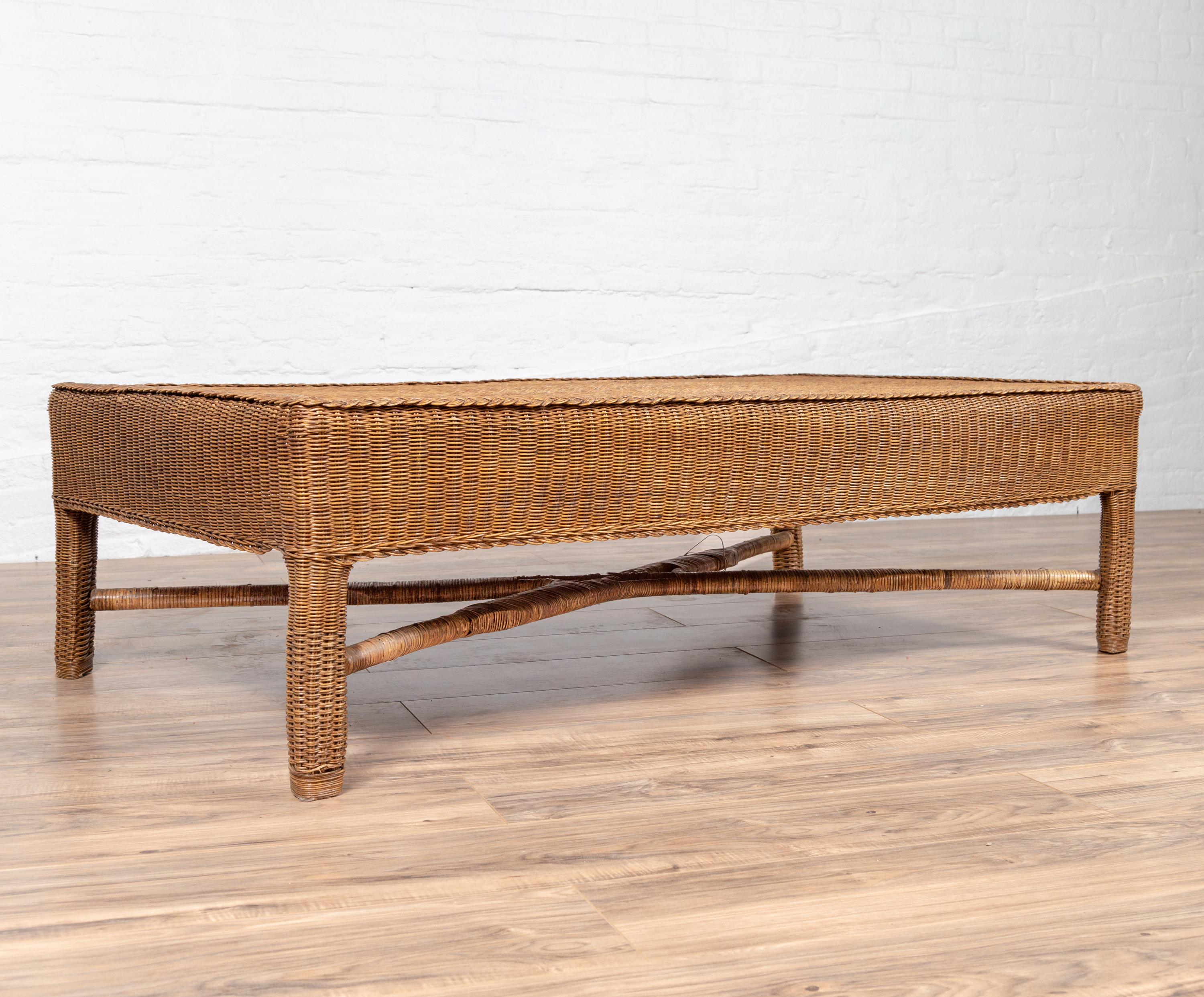 A vintage Burmese rattan coffee table from the mid-20th century, with X-form cross stretcher. Born in Burma during the midcentury period, this charming coffee table features a pure silhouette, completely adorned with rattan. A rectangular top sits