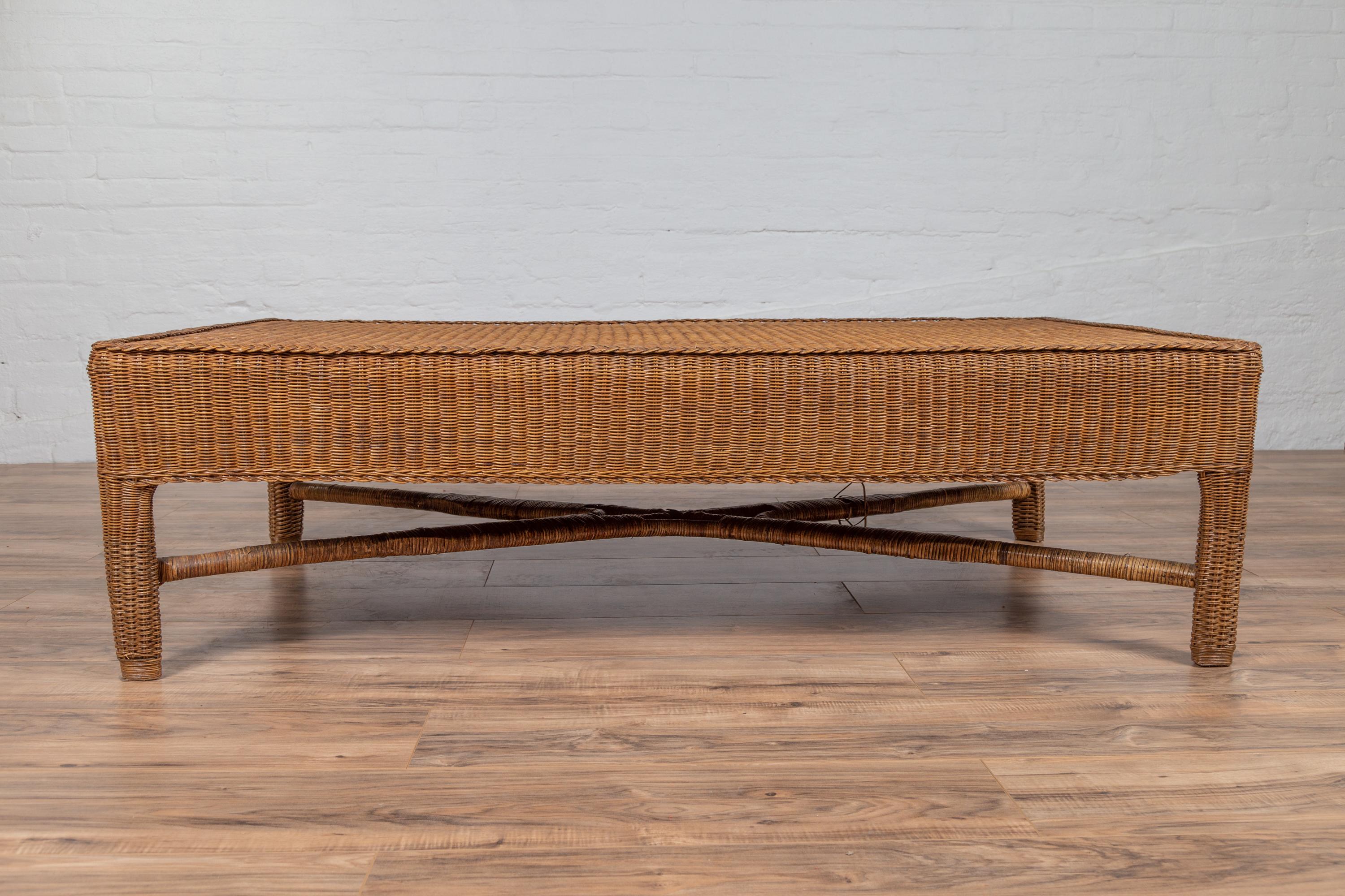 A vintage Burmese rattan coffee table from the mid-20th century, with X-form cross stretcher. Born in Burma during the midcentury period, this charming coffee table features a pure silhouette, completely adorned with rattan. A rectangular top sits