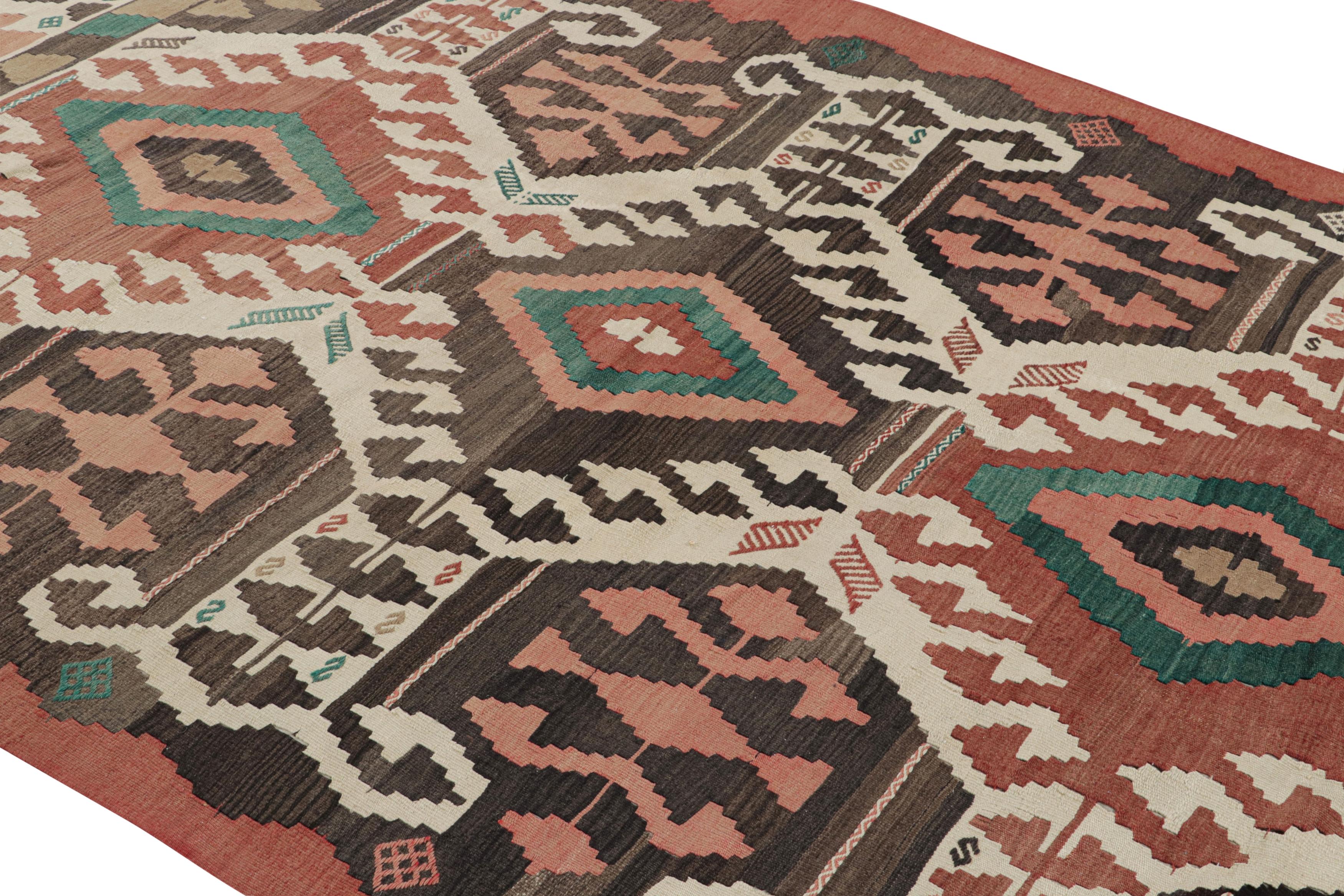 Handwoven in a wool flat weave originating from Turkey circa 1950-1960, this vintage Kilim rug connotes a midcentury tribal design of a rare colorway variation, sporting a prevailing pink and green accent to the beige-brown colorway in this