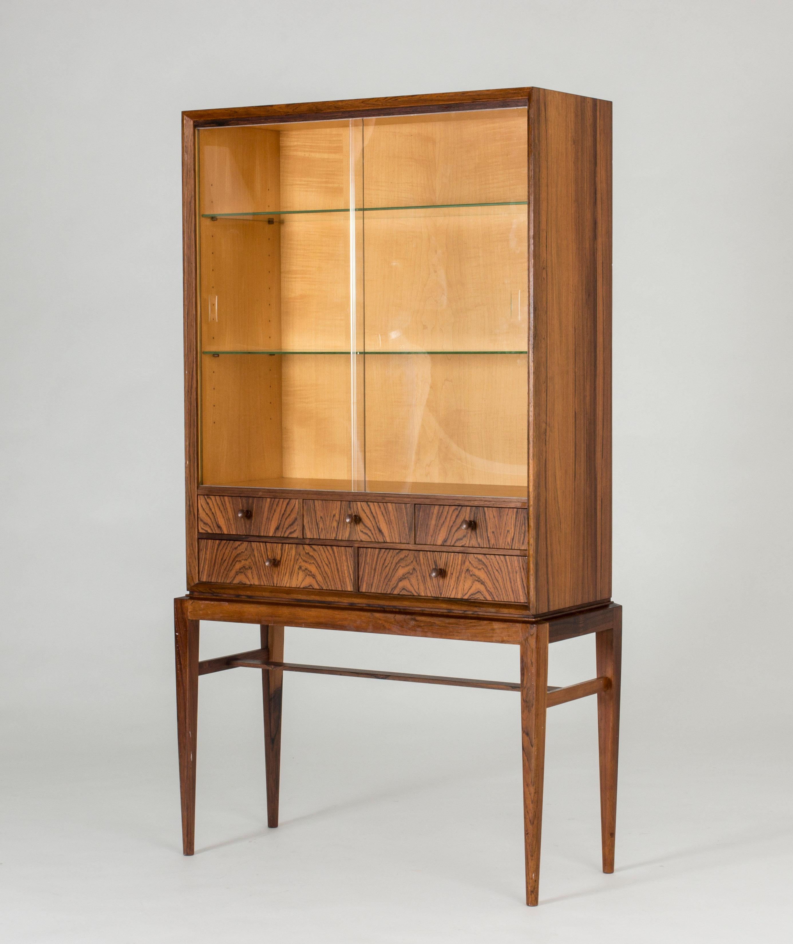 Elegant rosewood cabinet with vitrine doors and glass shelves by Svante Skogh. Small drawers with beautiful woodgrain. Slender legs give the cabinet a light expression.