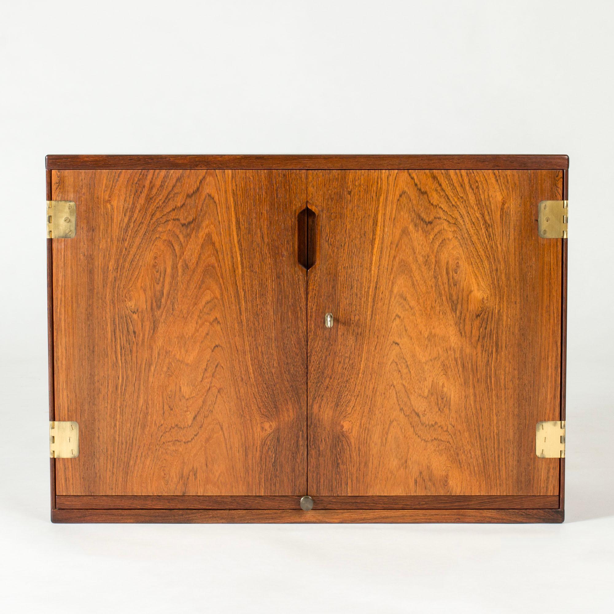 Amazing rosewood wall cabinet by Svend Langkilde with cool details of accentuated brass hinges and sculpted inset handle. Elegantly designed inside with shelves for glasses and a shelf that can be pulled out.