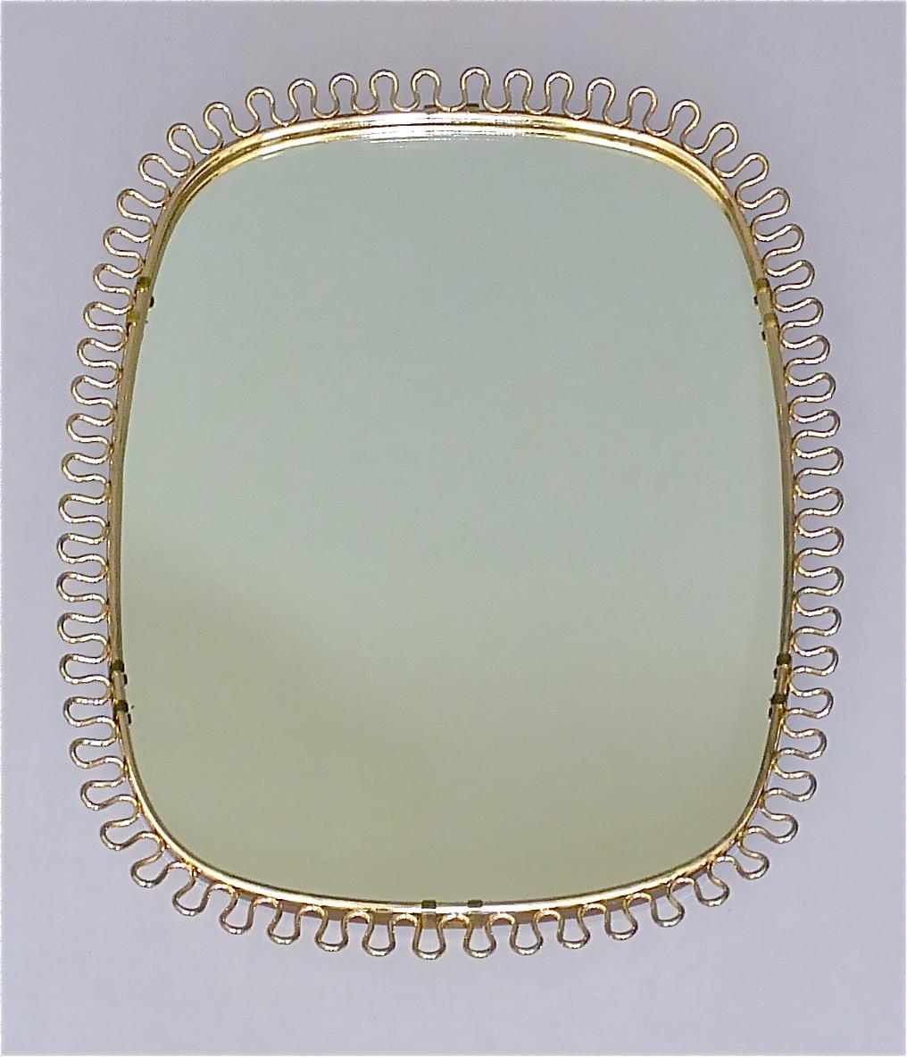 Sculptural and elegant midcentury wall mirror by Josef Frank Austria or Sweden for Svenskt Tenn, circa 1940s-1950s which is made of patinated brass metal, a beautiful brass loop-wire-decoration, original mirror glass, solid wood at the back and its