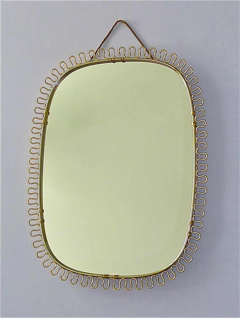 Sculptural and elegant midcentury wall mirror by Josef Frank Austria or Sweden for Svenskt Tenn, circa 1940s-1950s which is made of patinated brass metal, a beautiful brass loop-wire-decoration, original mirror glass, solid wood at the back and its