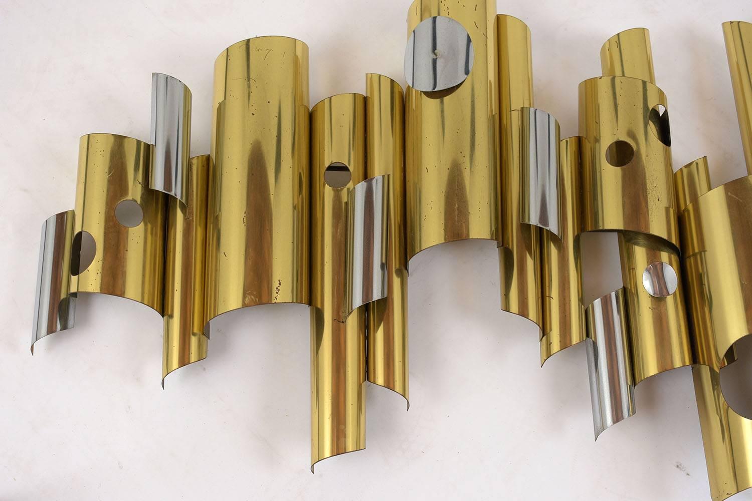 This 1960s Mid-Century Modern style wall sculpture is by C. Jere. The sculpture features brass and chrome cylinders in different sizes and lengths with cut out details. This sculpture is sturdy, stunning, and ready to be hung on any wall for years