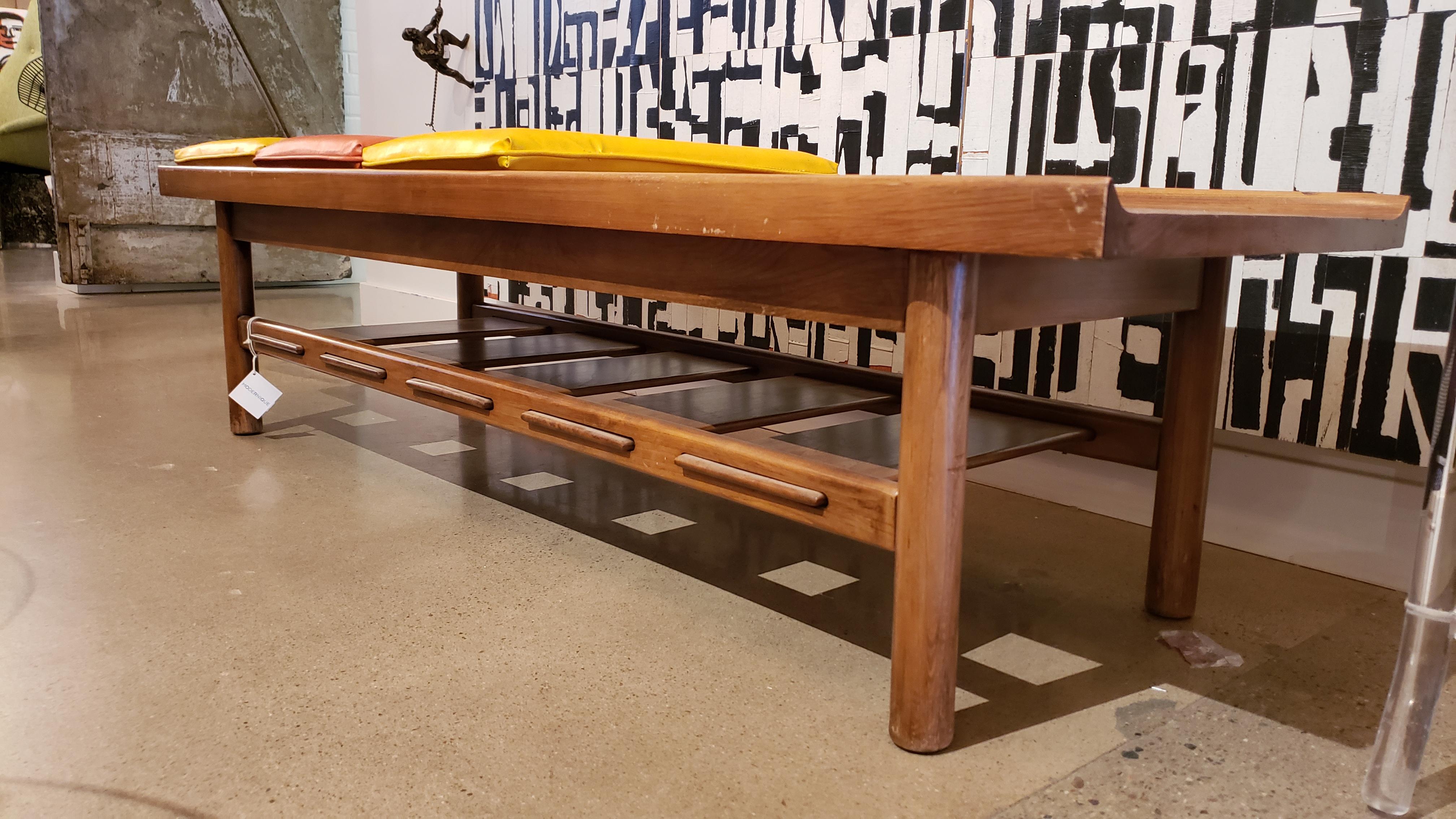 This walnut wood bench is very heavy and substantial. It is arranged with three original vinyl cushions in orange and yellow- characteristic colors of the 1950s.