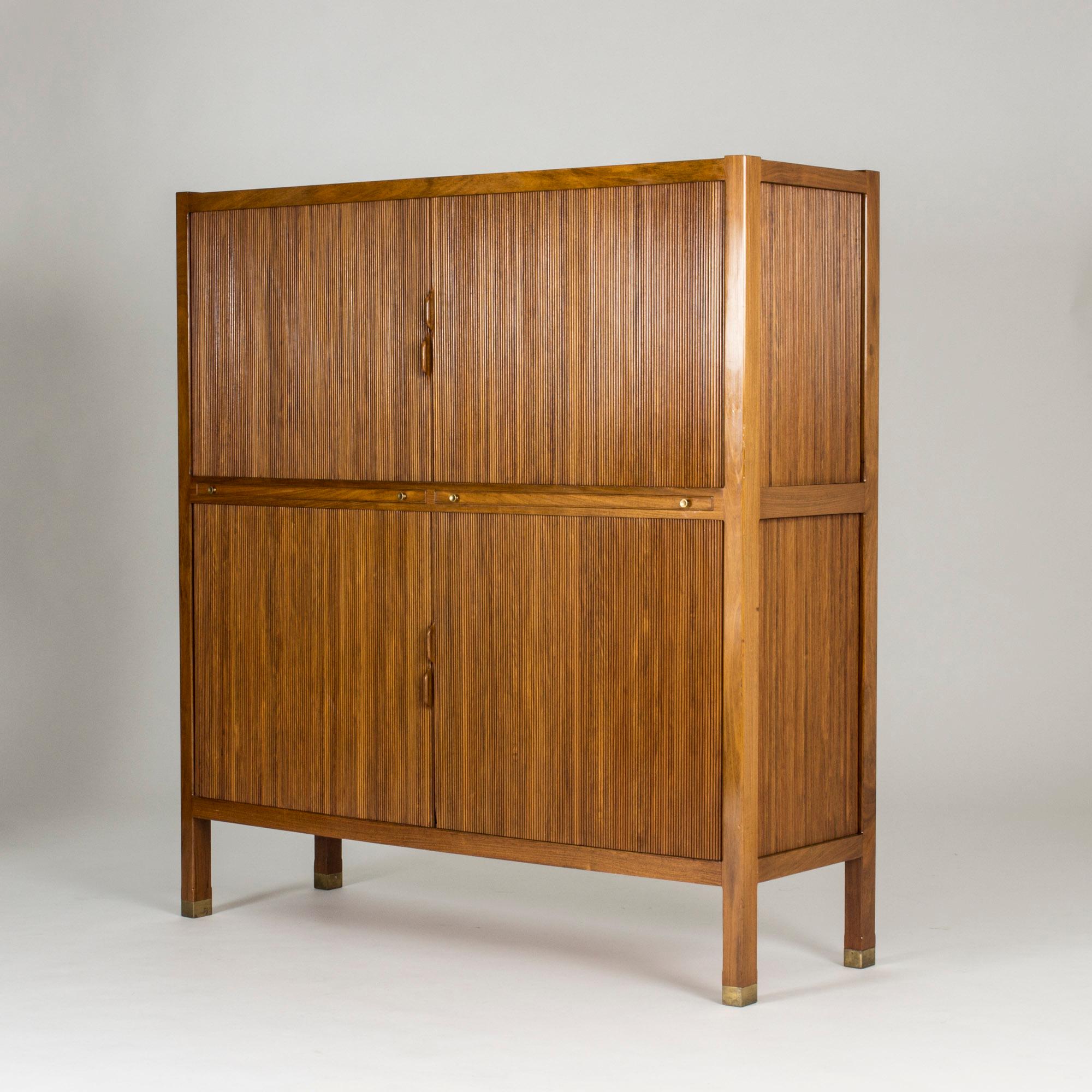 Stunning walnut cabinet by Carl-Axel Acking, masterfully produced by NK. Jalousie doors and beautifully crafted handles. The shelves that can be drawn out have brass strip inlays around the edges. Brass feet.

When Nordiska Kompaniet started to