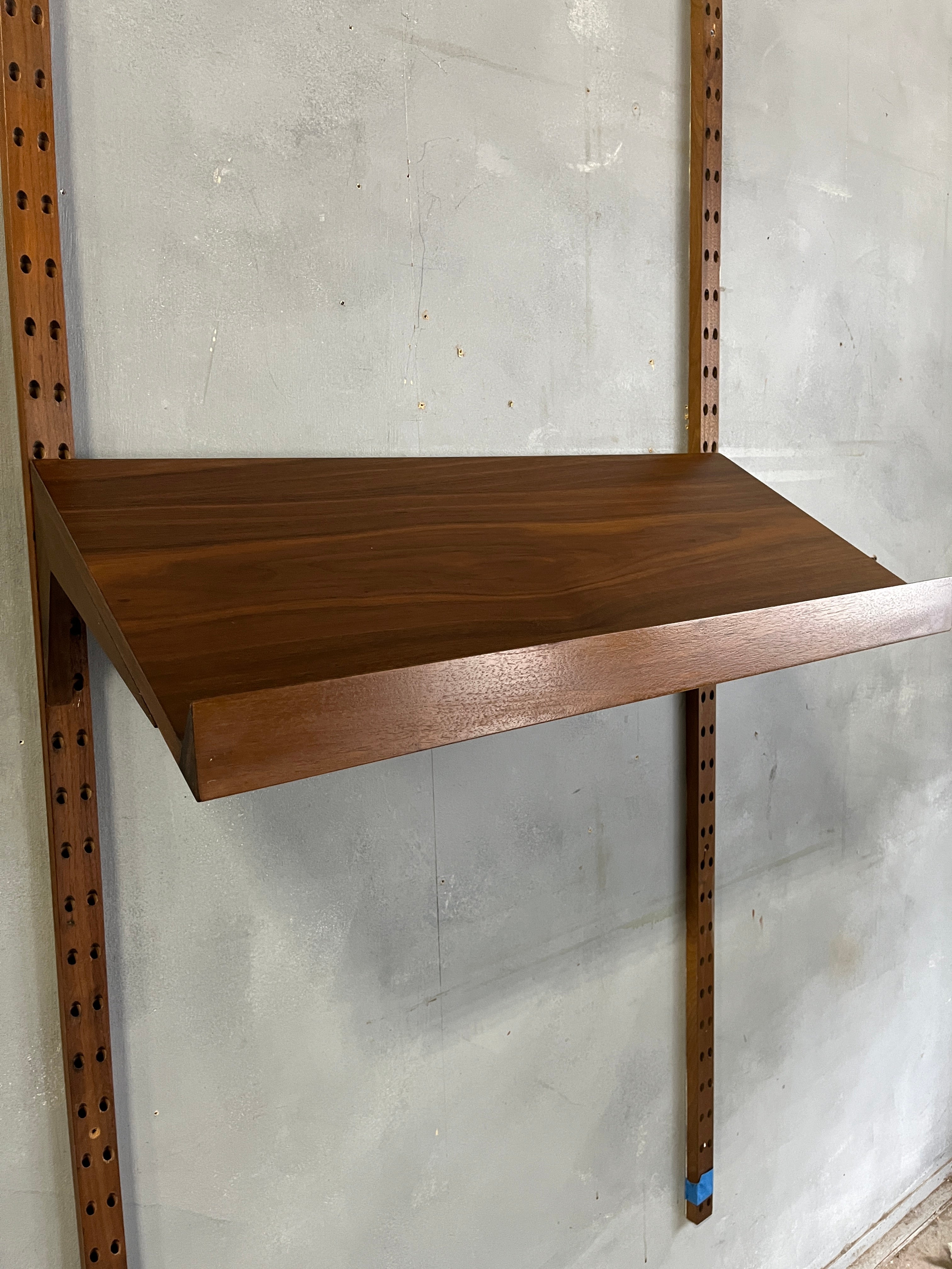 Beautiful  Walnut Cado System display shelf thats meant to hold books or flat artwork. The shelf has a beautiful catch at the bottom preventing a book from falling off. The wood brackets are also angled down. Please specify if your unit is darker or