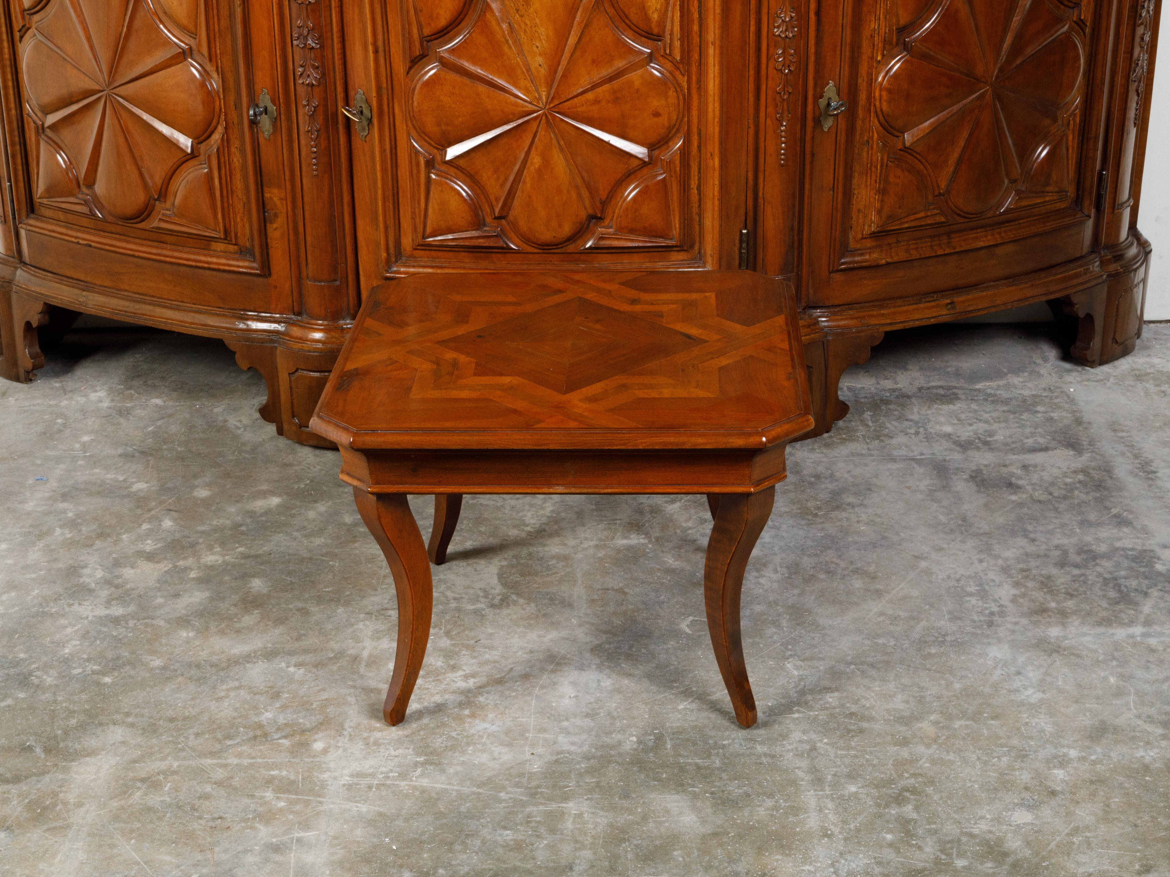 A walnut coffee table from the mid 20th century, with geometric star-inlaid top and curving legs. Created during the Midcentury period, this coffee table captures our attention with its square top with star inlay and canted corners, sitting above