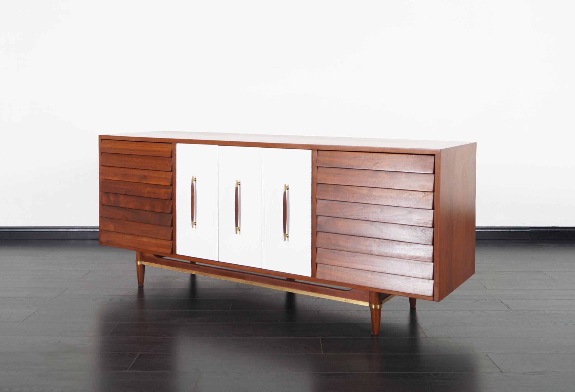 Midcentury walnut credenza designed by Merton Gershun for American of Martinsville. Features a total of nine dovetail drawers, three drawers are hidden behind white lacquer Bi-Folding doors.