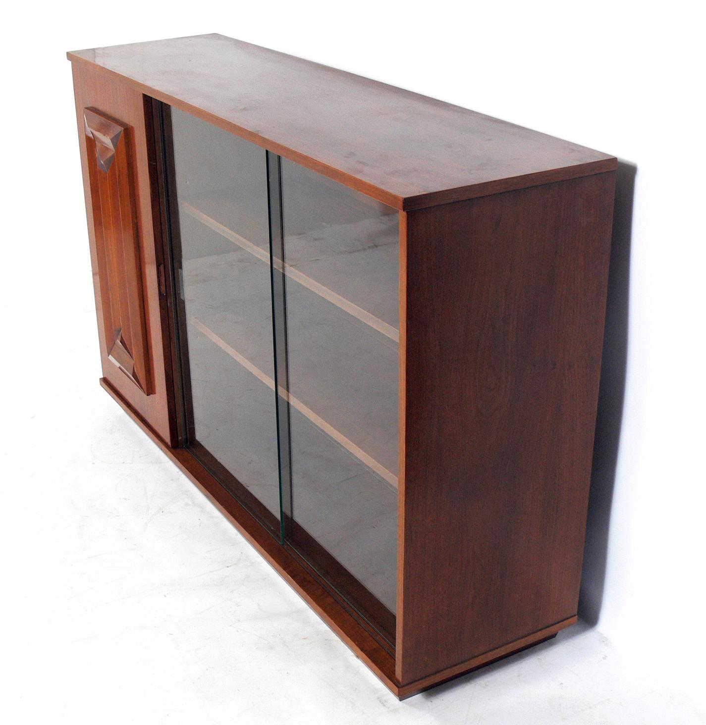 Midcentury walnut credenza or display cabinet with a geometric carved door, design attributed to Edmund Spence, circa 1950s. This piece is currently being refinished and can be completed in your choice of finish color. The price noted below includes