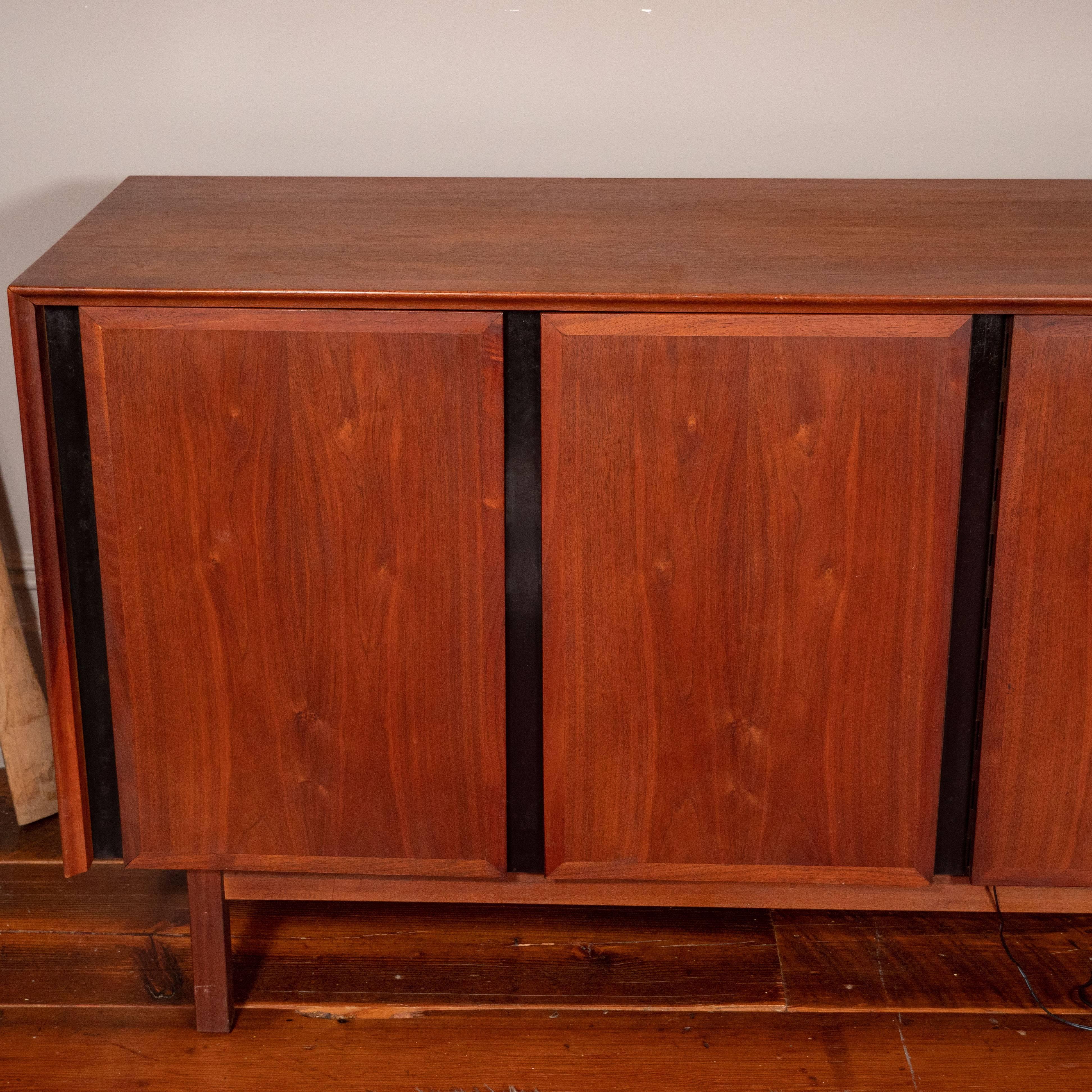 Midcentury walnut credenza sideboard by Merton Gershun for Gillingham, circa 1970s.
Left doors open to three enclosed drawers. Right side doors reveal open shelves. Dillingham sticker present.
Some fading/wear to finish on top. Scuffs on legs.
 