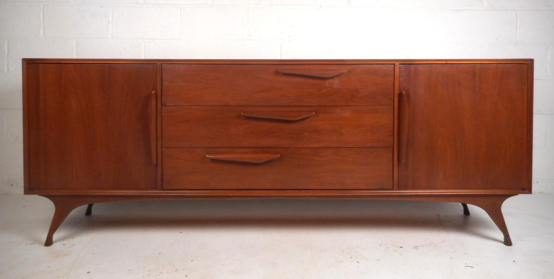 This beautiful vintage modern credenza features nine large drawers with six of them hidden by cabinet doors. This unique case piece has sculpted horizontal pulls on the centre drawers that graduate downward on an angle. Gorgeous walnut wood grain,