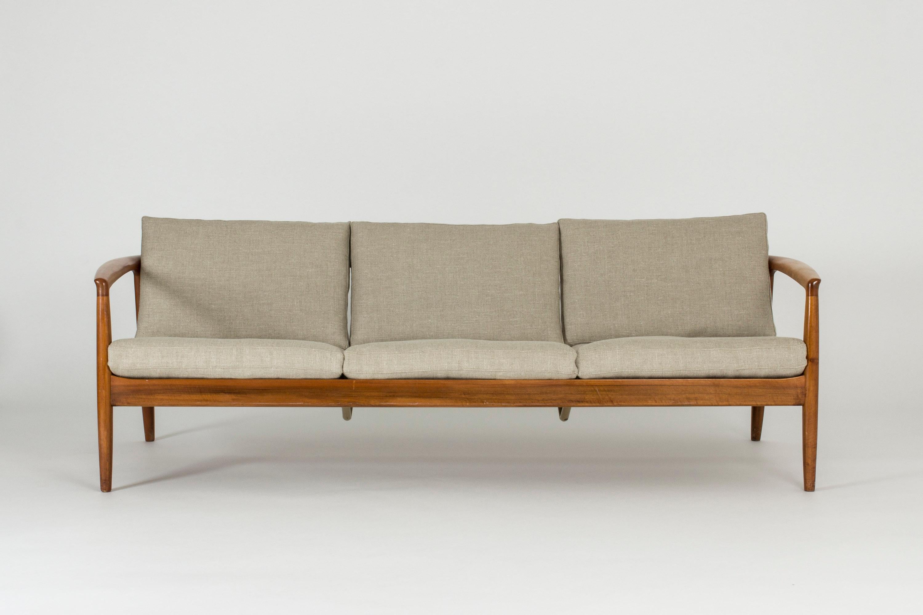 Cool and comfy sofa by Folke Ohlsson in luxurious walnut. Beautiful ribbed back and curved armrests that. Reupholstered with a sand colored linen fabric.