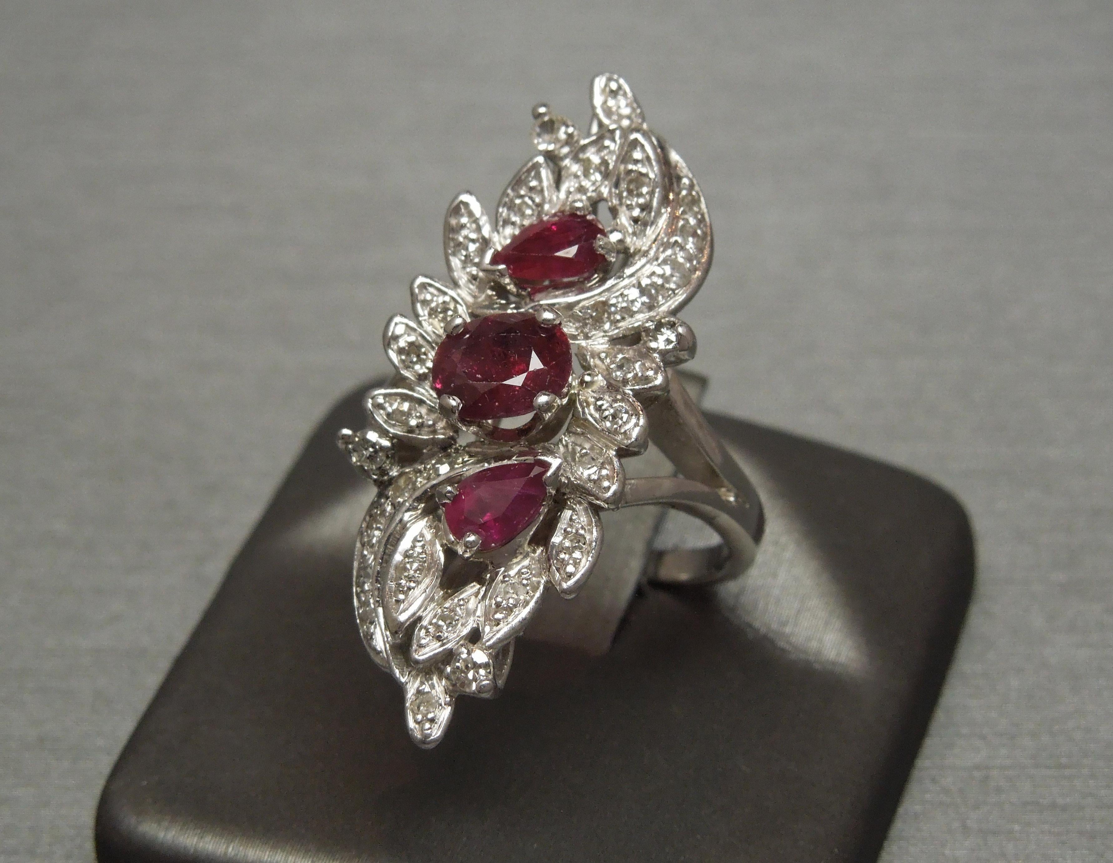 This Ruby Bouquet Ring features three focal Natural Medium Red Rubies (slightly opaque) - a central 1 carat Oval cut with 2 slightly smaller Pear cuts totaling 0.75 carats. Ruby is noted as the 
