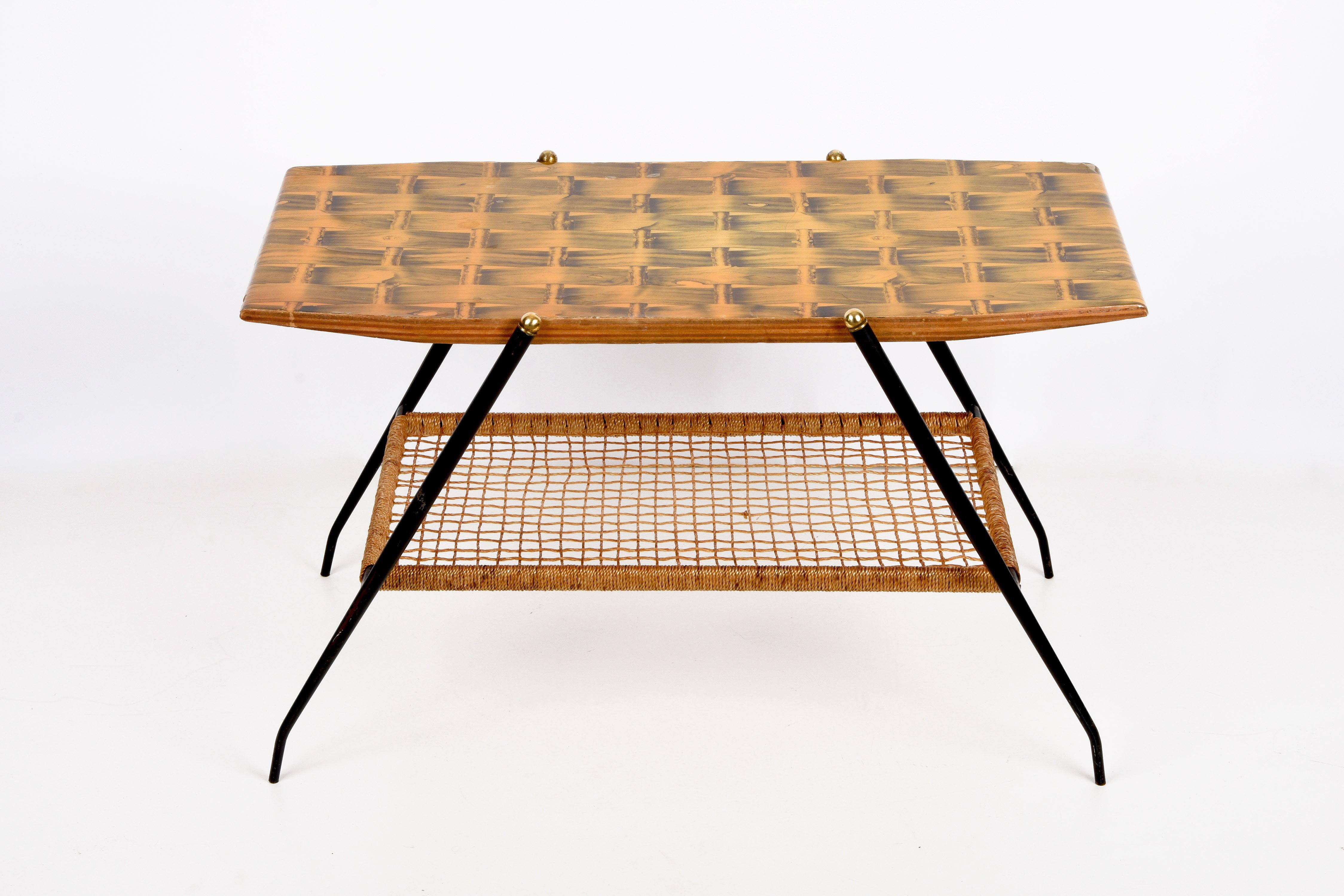 Marvellous midcentury coffee table in wood, brass and black metal. This table was produced in Italy during the 1950s.

It is a rare and elegant wooden coffee table with glazed braided print, it has black metal legs with a wonderful nylon magazine