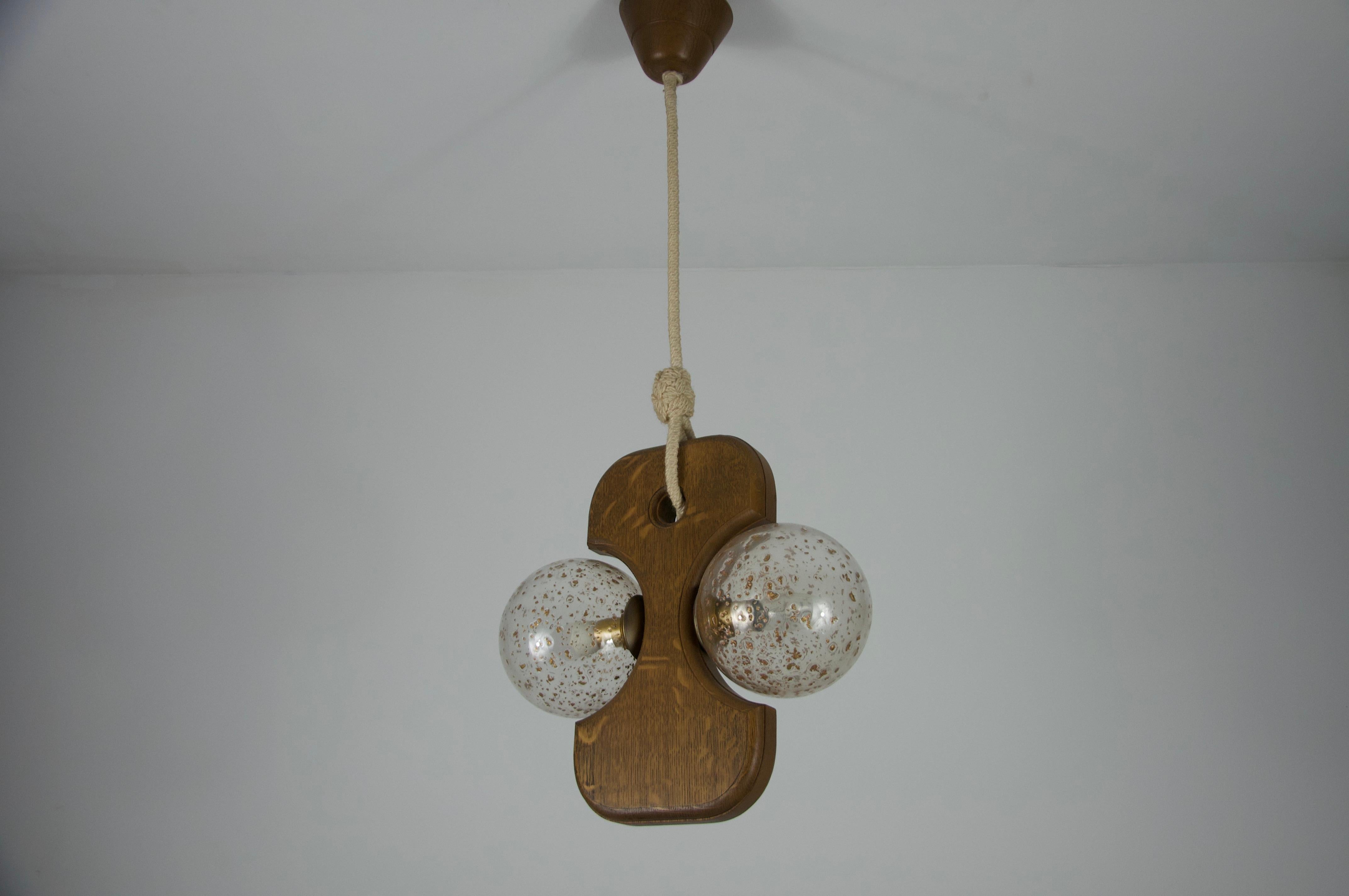 This hanging lamp by Temde from the 1960s is a striking example of Mid-century modern design. It features a unique, sculptural wooden frame that holds two spherical glass globes. The wood, likely teak or a similar warm-toned species, is beautifully