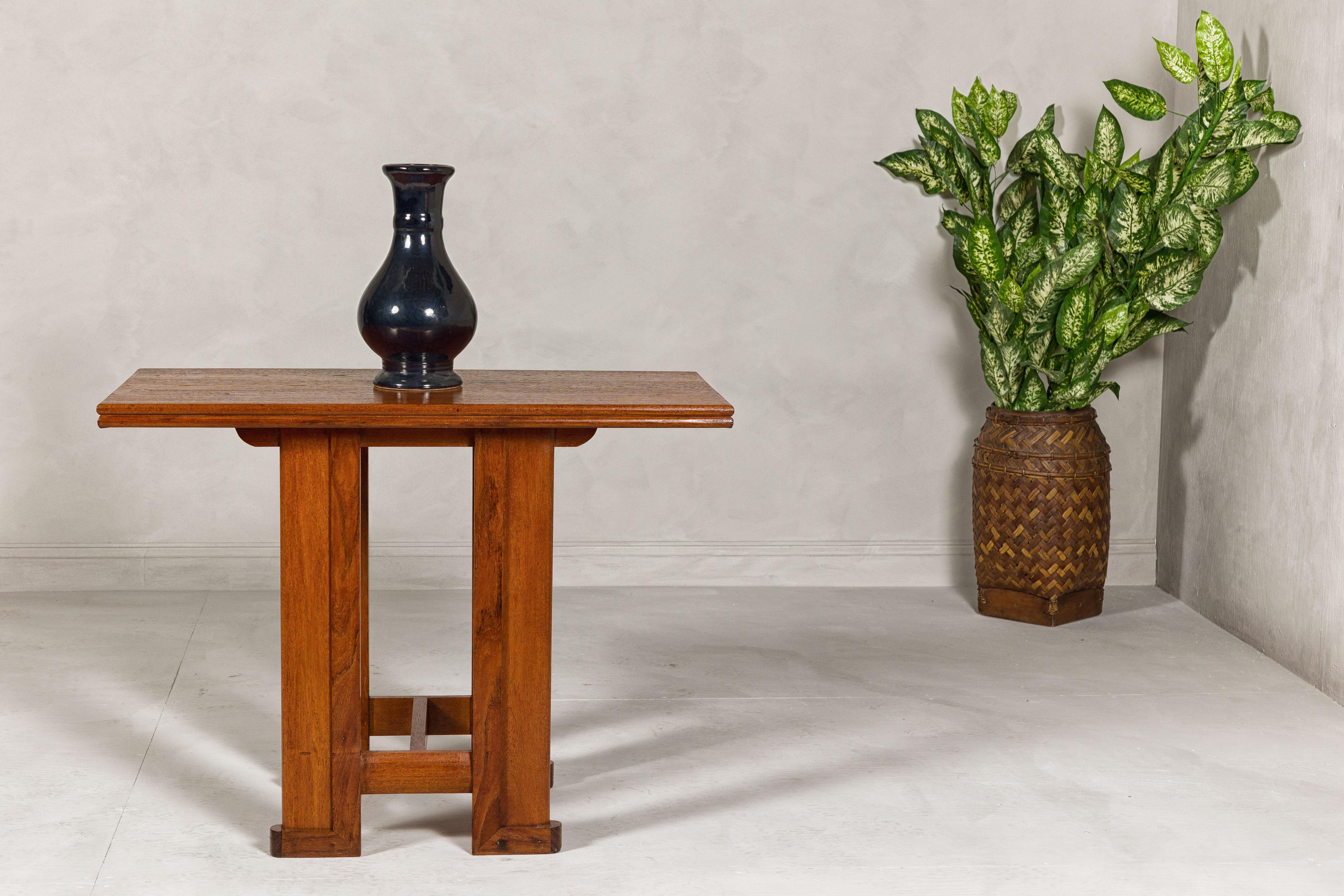 A Midcentury wooden console table with Art Deco inspired base. This midcentury wooden console table, gracefully restored and refinished, offers a nod to Art Deco elegance with its linear base. The table's streamlined design and brown surface reflect
