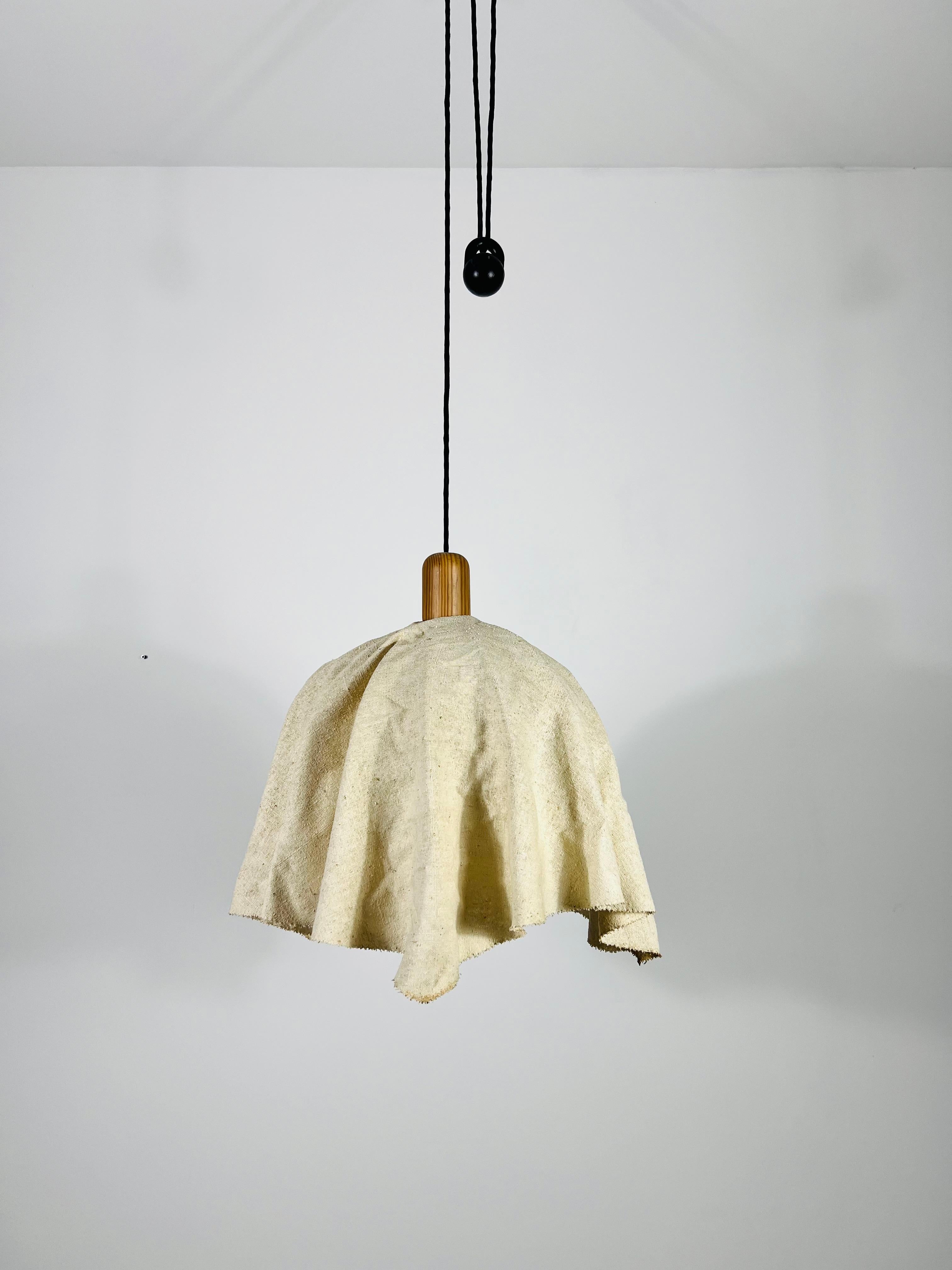 This adjustable hanging lamp, crafted by Domus in the 1960s, features a counterweight mechanism that allows you to adjust its height from 100 to 180 cm. By pulling the wooden handle within the fabric lampshade, you can easily raise or lower the