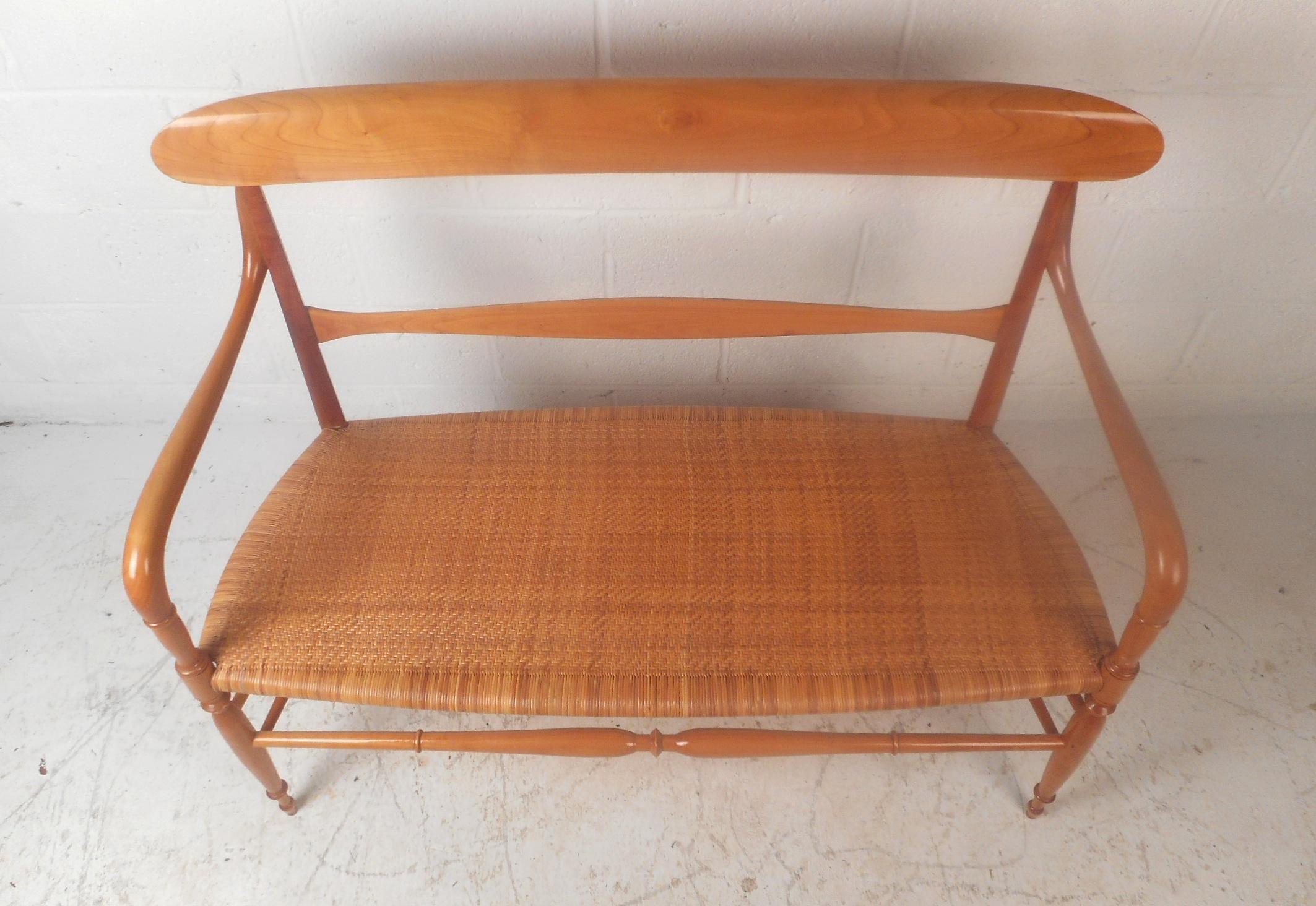 A wonderful vintage modern settee with a woven cane seat and a sculpted frame. The sleek design has a tightly woven cane seat ensuring a comfortable and sturdy place to sit. The carved stretchers, smooth curved arm rests, and tapered legs show true