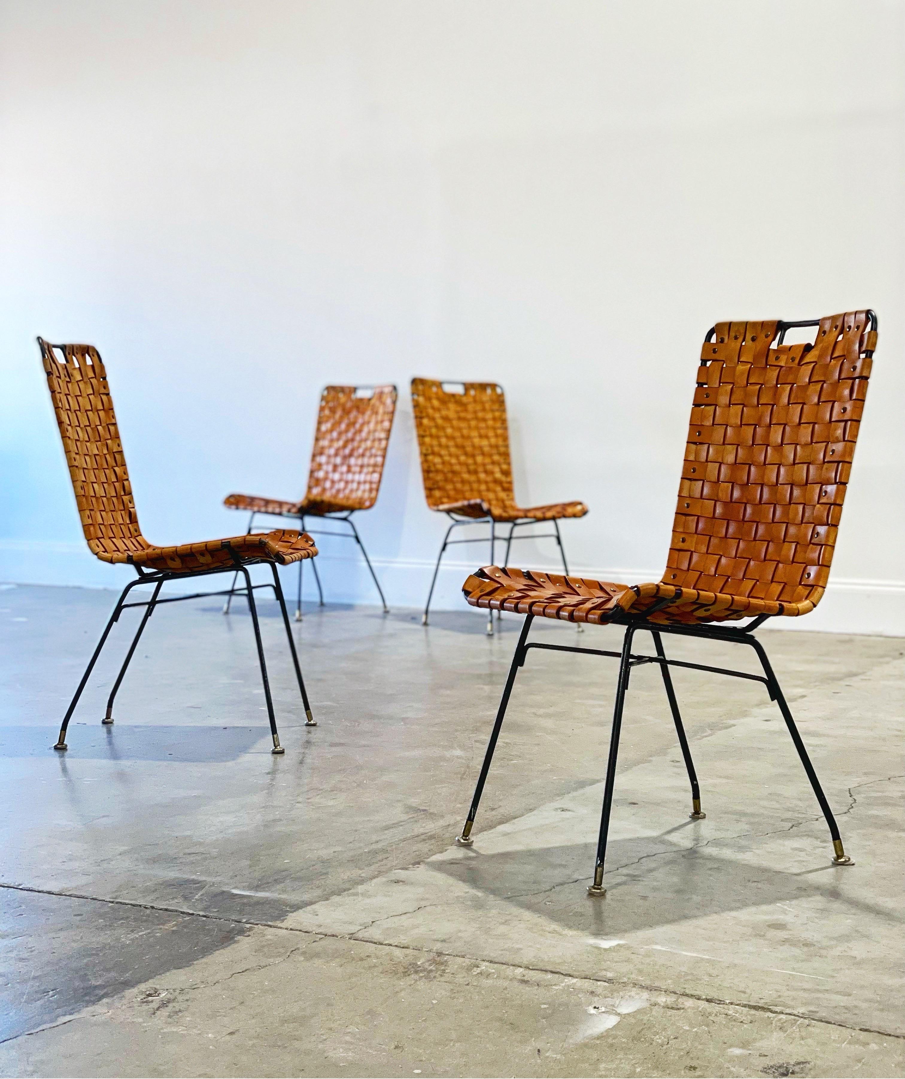 Set of four wrought iron and woven leather side chairs by Arthur Umanoff for Shaver Howard. Gorgeous cognac tone leather has aged to perfection and displays a warm rich patina. Iron frames are sound and secure. All leather straps are intact - no