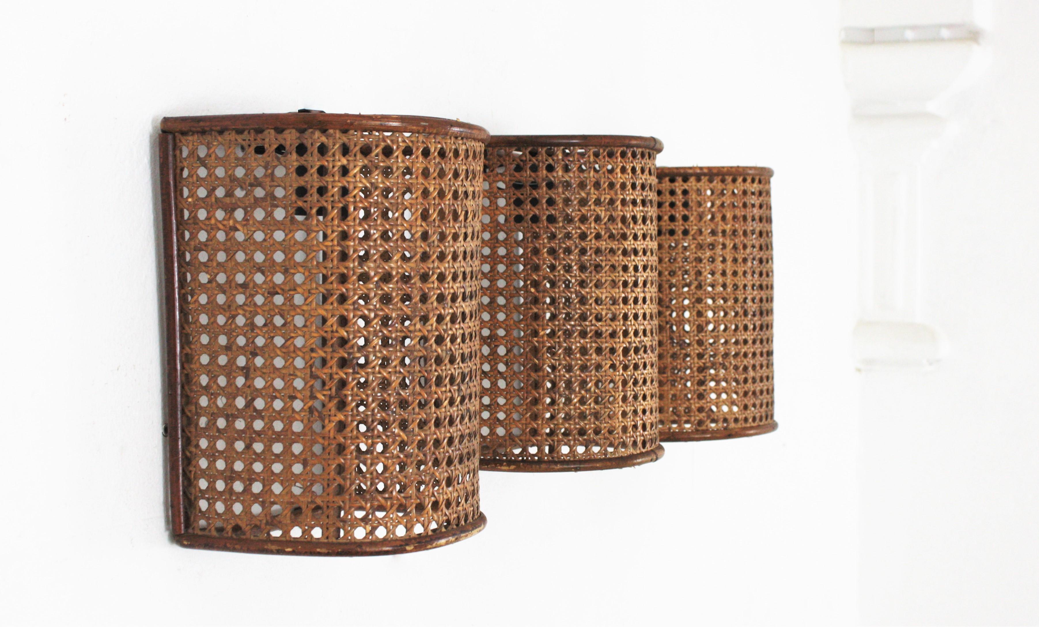 Set of three half cylinder wall lights with wicker and rattan woven shades, Italy, 1960s.
These light fixtures are made with wicker basket weave panel on a rattan semi cylindrical structure.
They will be the perfect choice to add a Modernist but