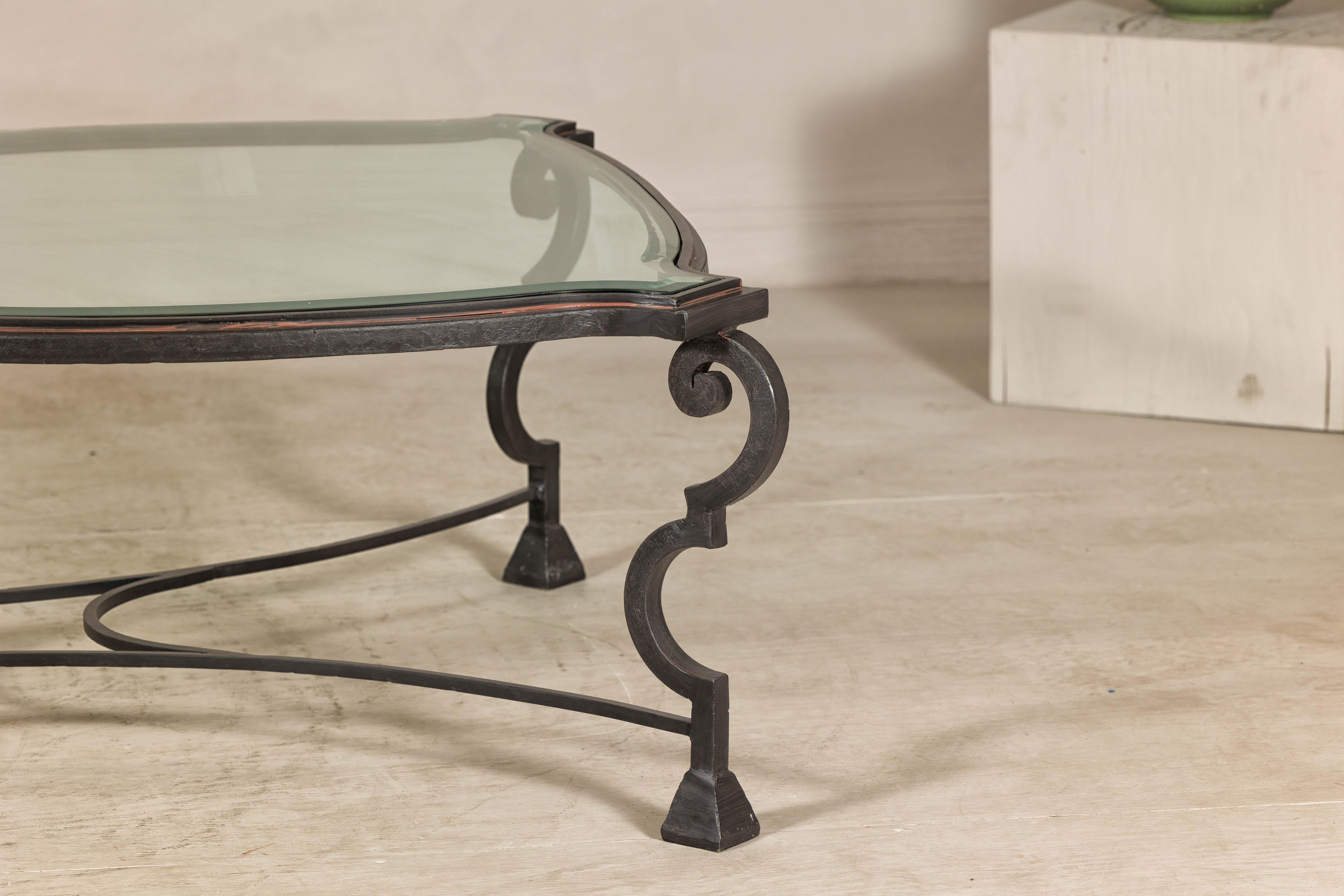 Table basse vintage en fer forgé avec pieds en S et plateau en verre. Cette table basse vintage en fer forgé, datant d'entre 1940 et 1960, incarne un mélange intemporel d'élégance et de durabilité. La base est fabriquée en fer forgé et présente des