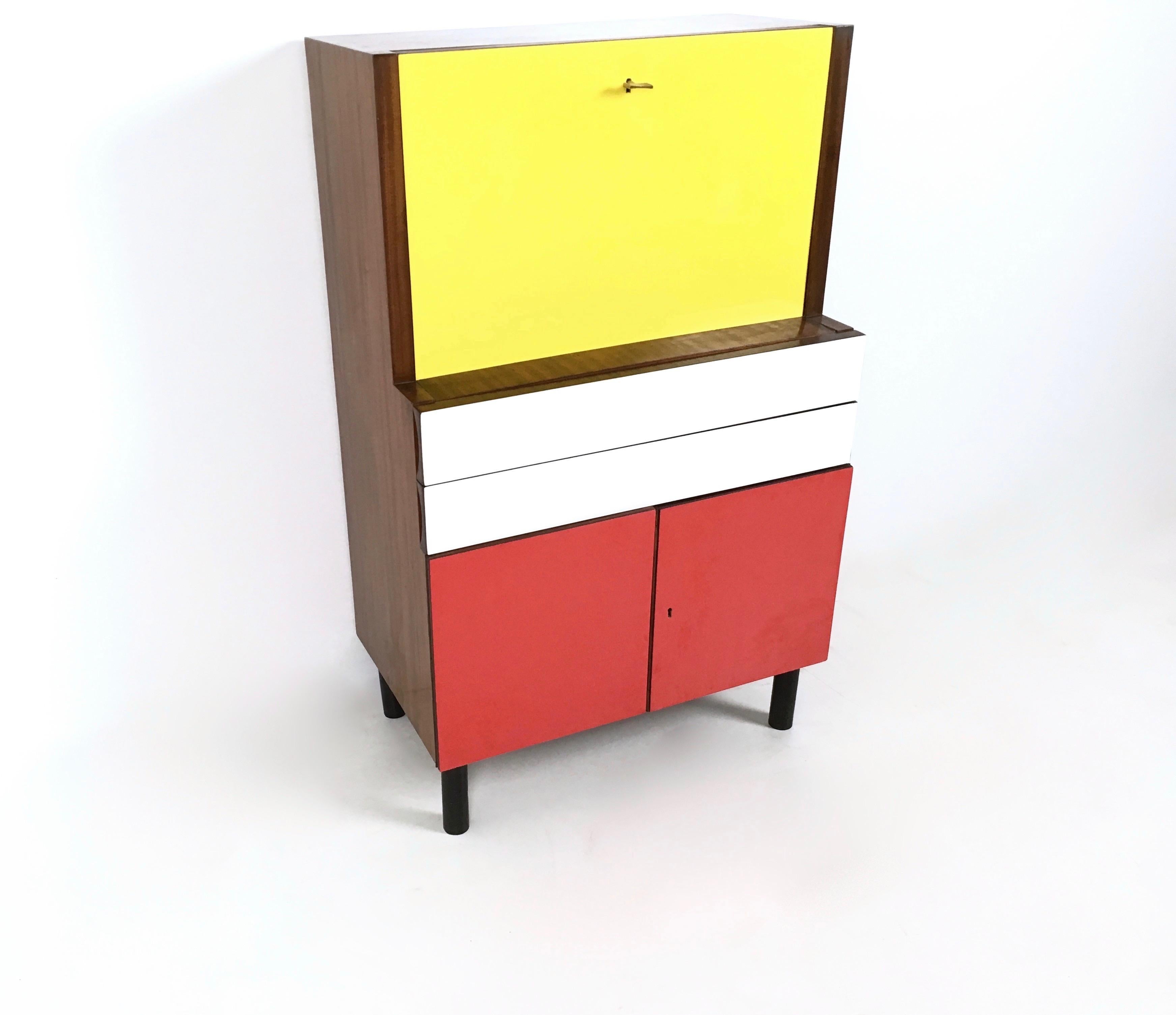 This secretaire features yellow, white and red formica sheets, one glass shelf and a back-painted glass top. 
It may show slight traces of use since it's vintage, but it can be considered as in very good original condition and ready to become a