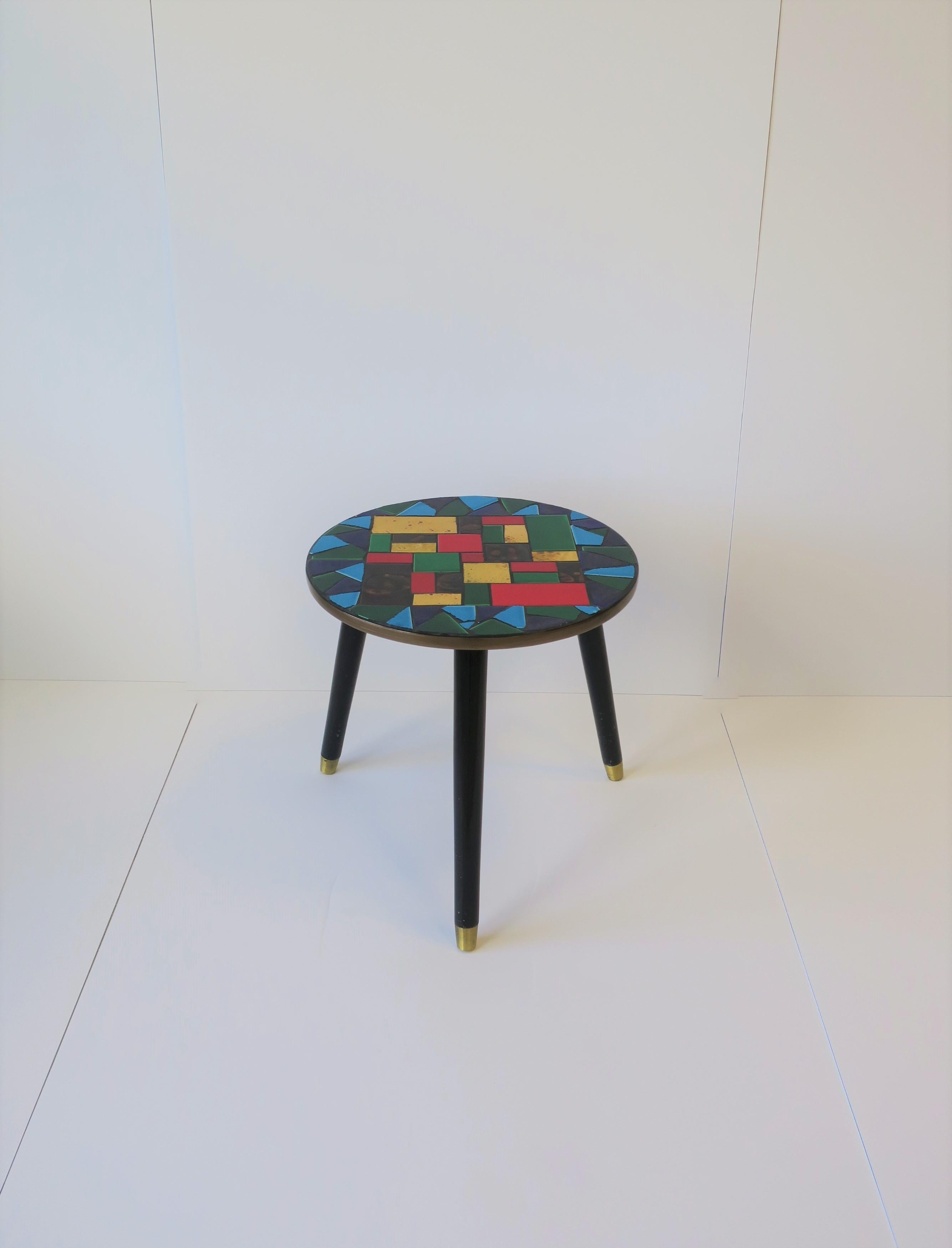 A very beautiful Mid-Century Modern period tile mosaic round side table with black tripod wood base, circa Mid-20th century, 1960s, Japan. Mosaic tile colors include: red, yellow, brown, green, royal blue and turquoise blue. 

Table measures: 15.75
