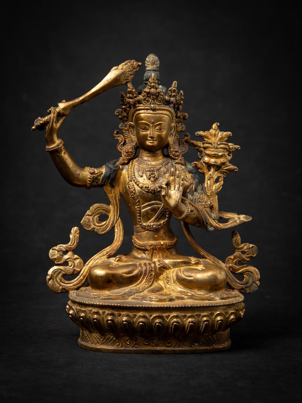 This old bronze Nepali Manjushri statue is a beautiful representation of Buddhist wisdom and artistry from the mid-20th century. Crafted from bronze and fire gilded with 24-karat gold, the statue stands 22.5 cm high, 17.5 cm wide, and 9.5 cm deep,
