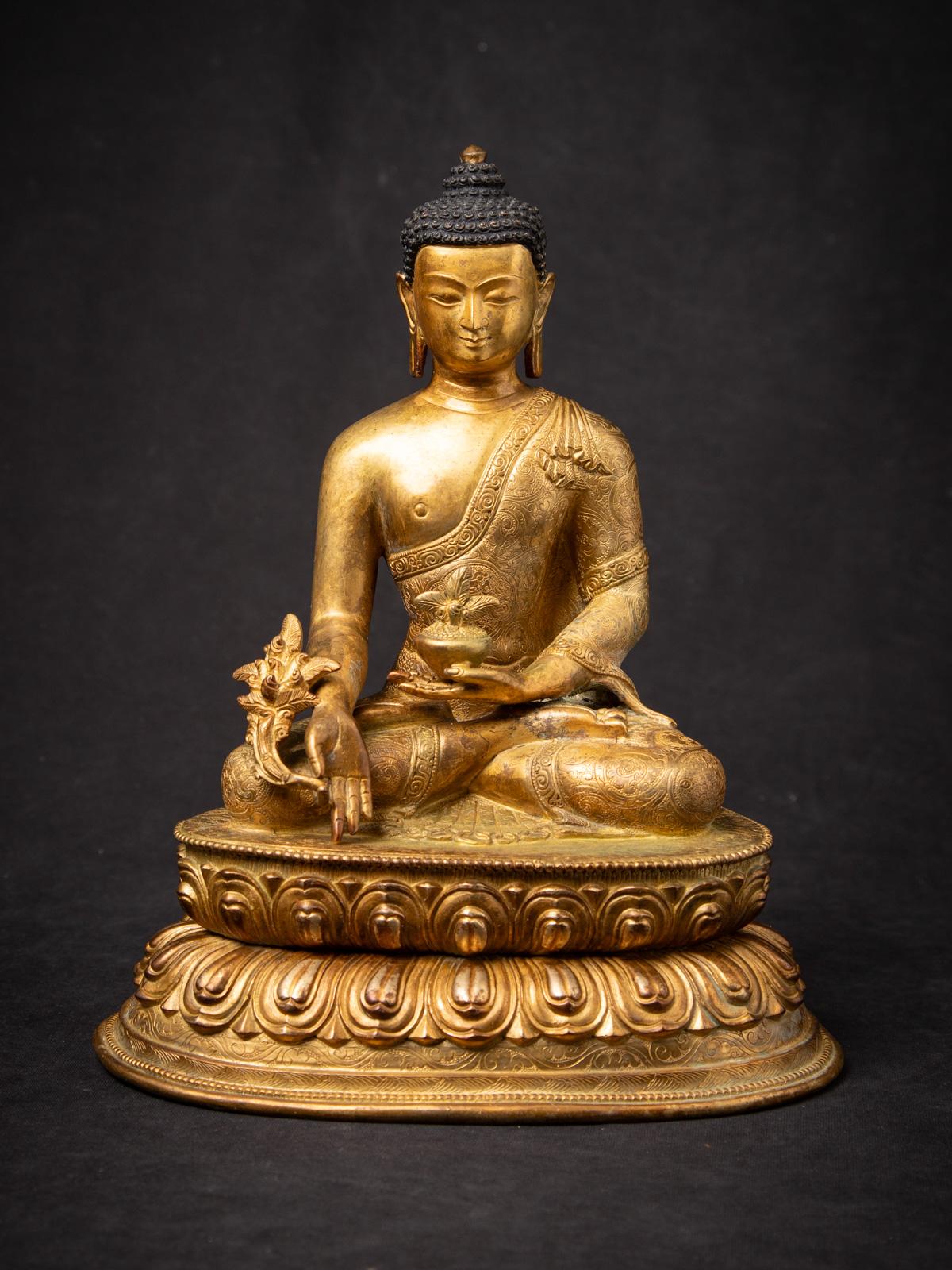 Esta antigua estatua de bronce del Buda de la Medicina nepalí es una pieza de alta calidad de la artesanía tradicional del Himalaya, de mediados del siglo XX y originaria de Nepal. Fabricada expertamente en bronce macizo y dorada al fuego con oro de
