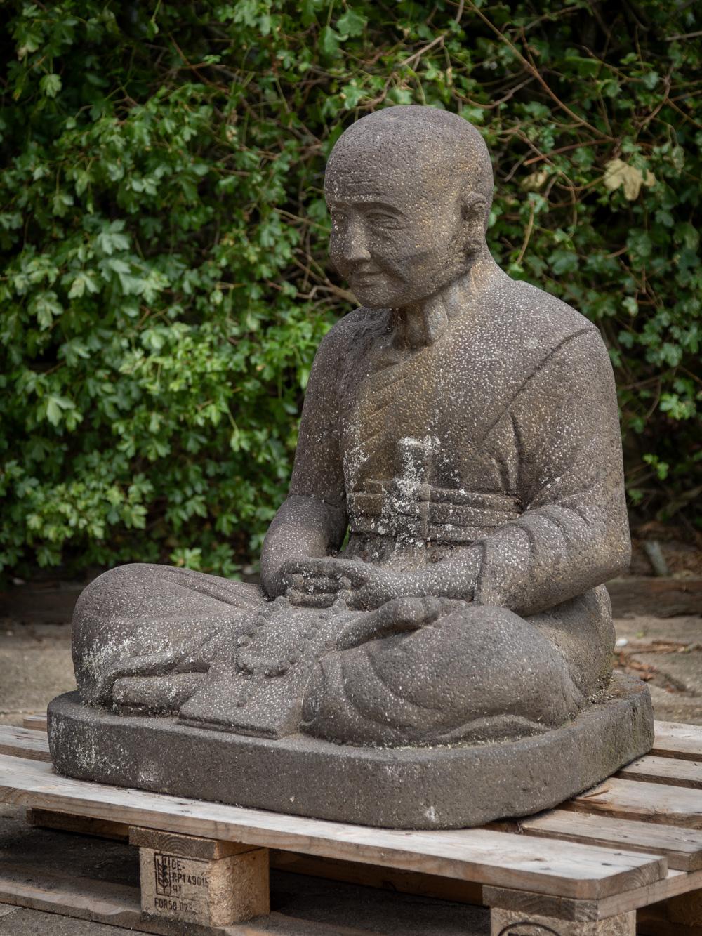 This old lavastone monk statue is a striking and substantial piece of art. Crafted from lavastone, it stands tall at 93 cm, with dimensions of 72 cm in width and 62 cm in depth. Its estimated weight is around 250 kg, showcasing the solid and