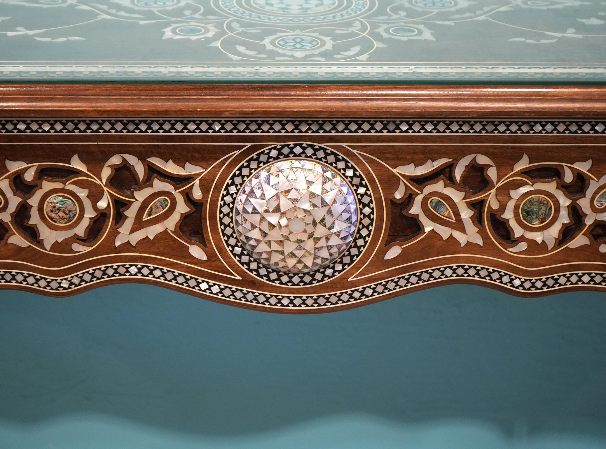 This elaborately inlaid Middle Eastern console table features a protective glass top above a stunning inlaid top with arabesques leaf work and rosettes. The tree drawer fronts center a raised convex rosette and continuous decoration in the shape of