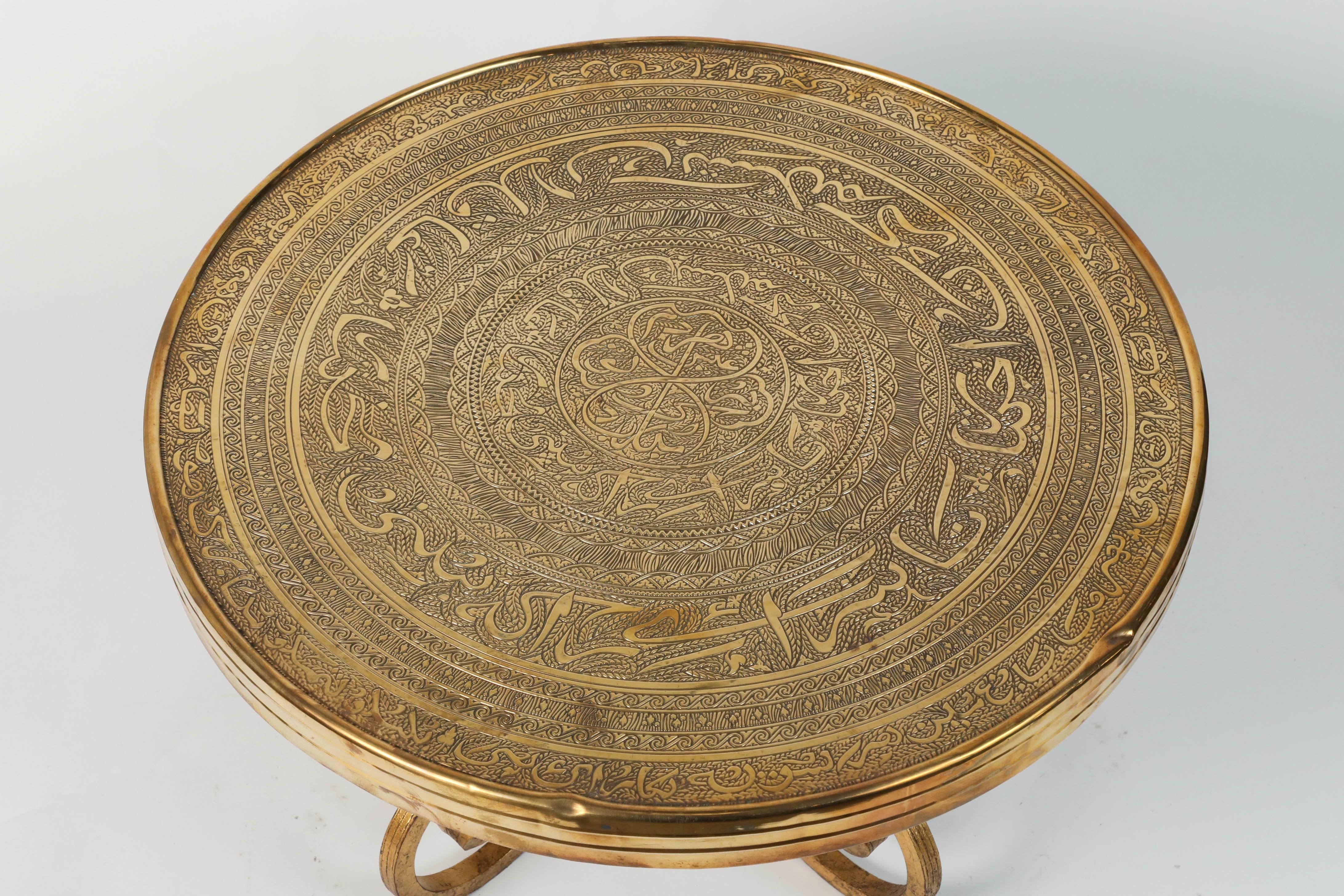 Middle Eastern Moorish antique brass repousse tray table with gilt iron stand.
The embossed Art Deco style brass top is decorated with Arabic calligraphy writing and repousse geometric Islamic Moorish designs.
The Arabic words are poetry from the
