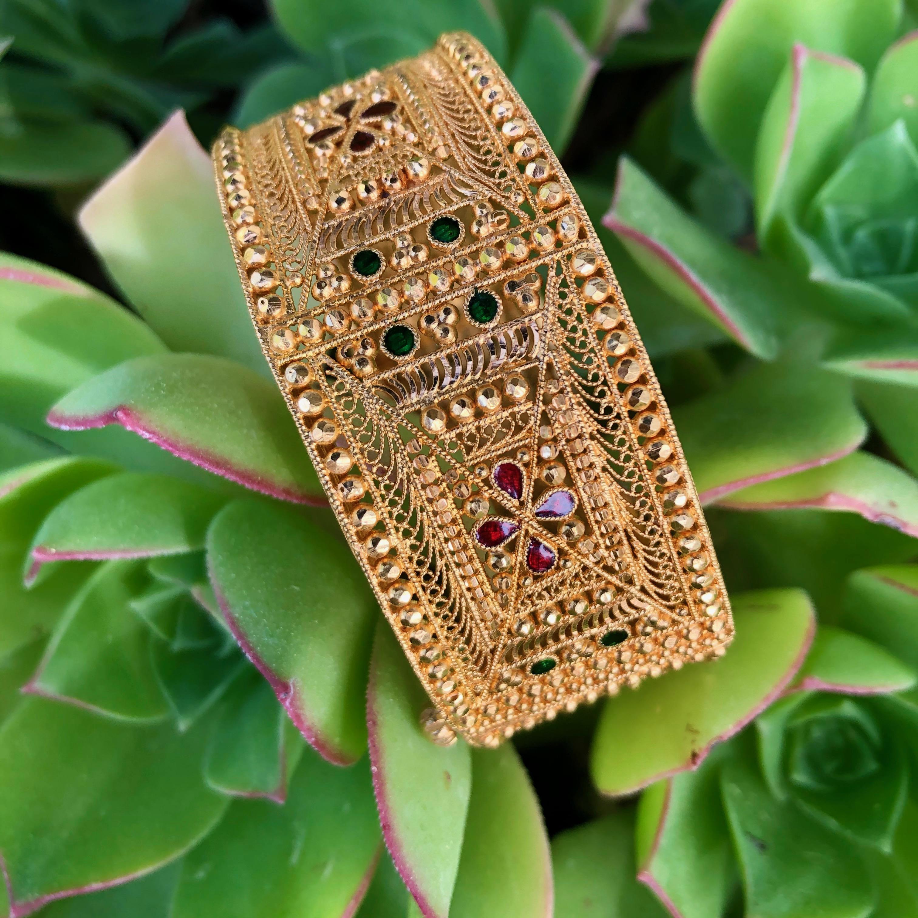 Hübsches Armband im orientalischen Stil aus 21 Karat Gelbgold. Das Armband hat ein verziertes Design mit filigranen Arbeiten, facettierten Perlen, handgravierten Kanten und kleinen Bereichen mit roter und grüner Emaille. Das Armband misst 25 mm in