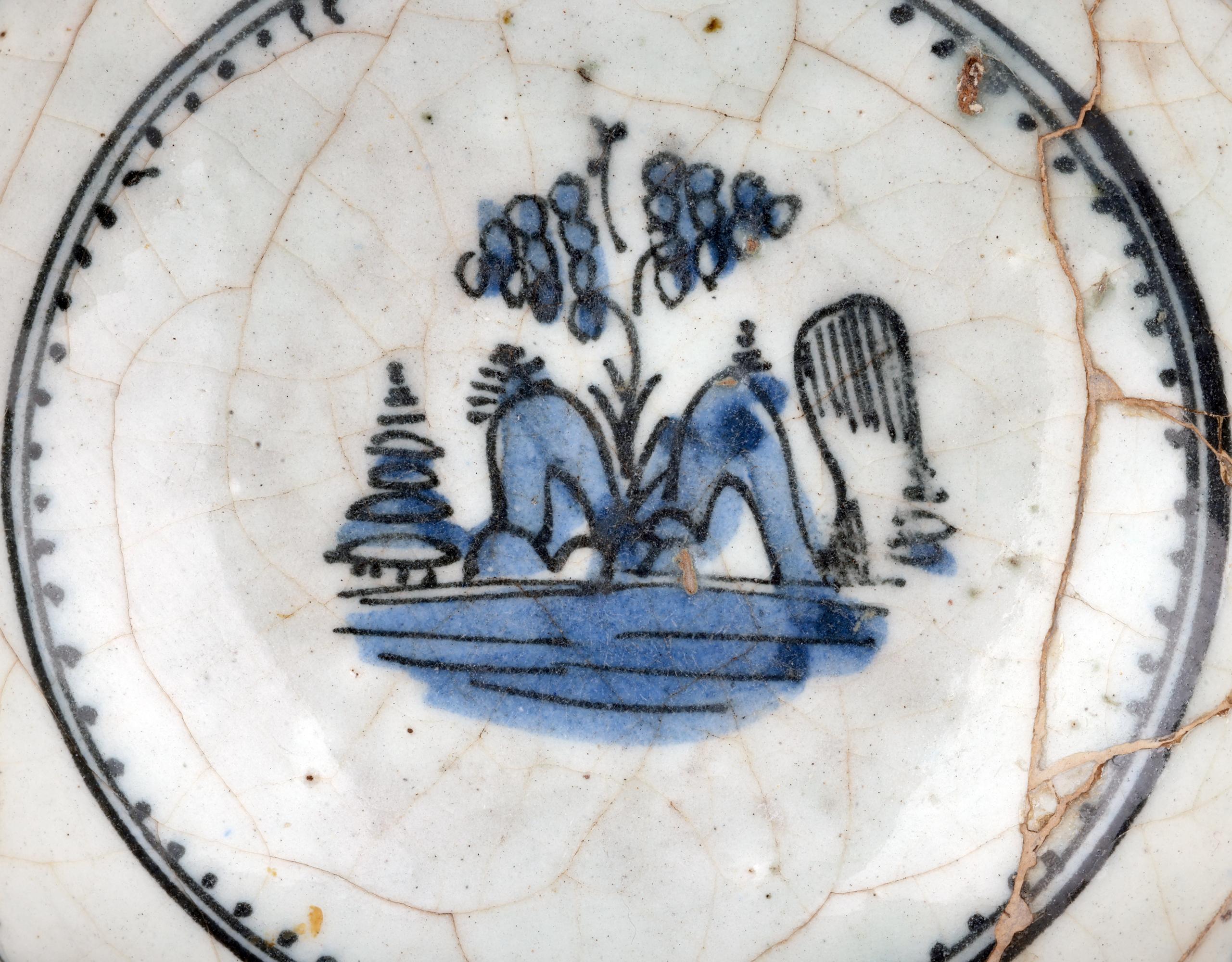 Inusual cuenco antiguo de cerámica islámica de Oriente Medio pintado a mano en azul y blanco con edificios estilizados y vegetación, que se cree que data del siglo XVII. El cuenco, ligeramente hecho a mano, se alza sobre un estrecho pie redondo con