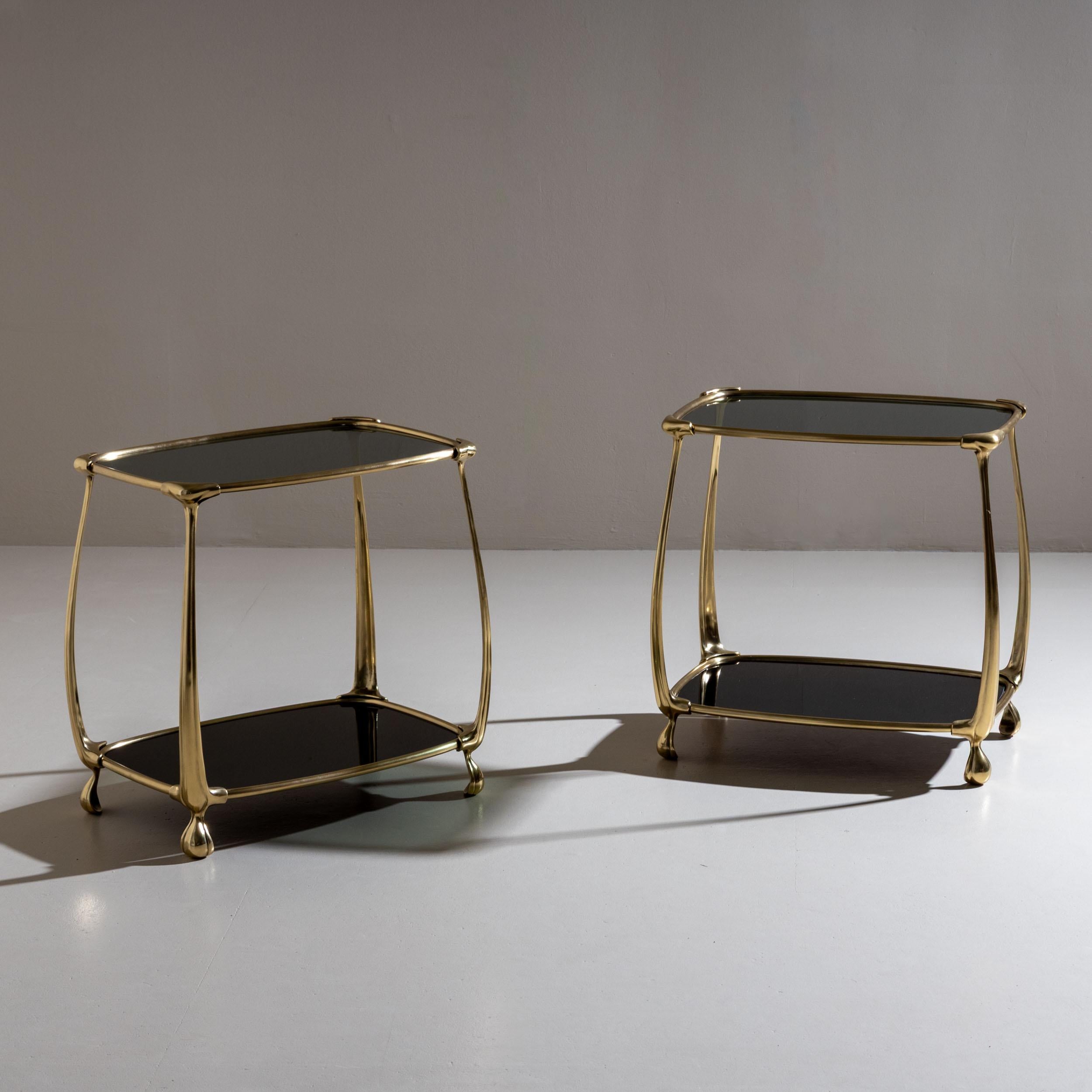 Elegant pair of side tables featuring organically shaped brass frames and two dark-tinted glass shelves each. The subtly trapezoidal form combined with the flowing design language recalls influences of Art Nouveau. Attributed to Fontana Arte, these