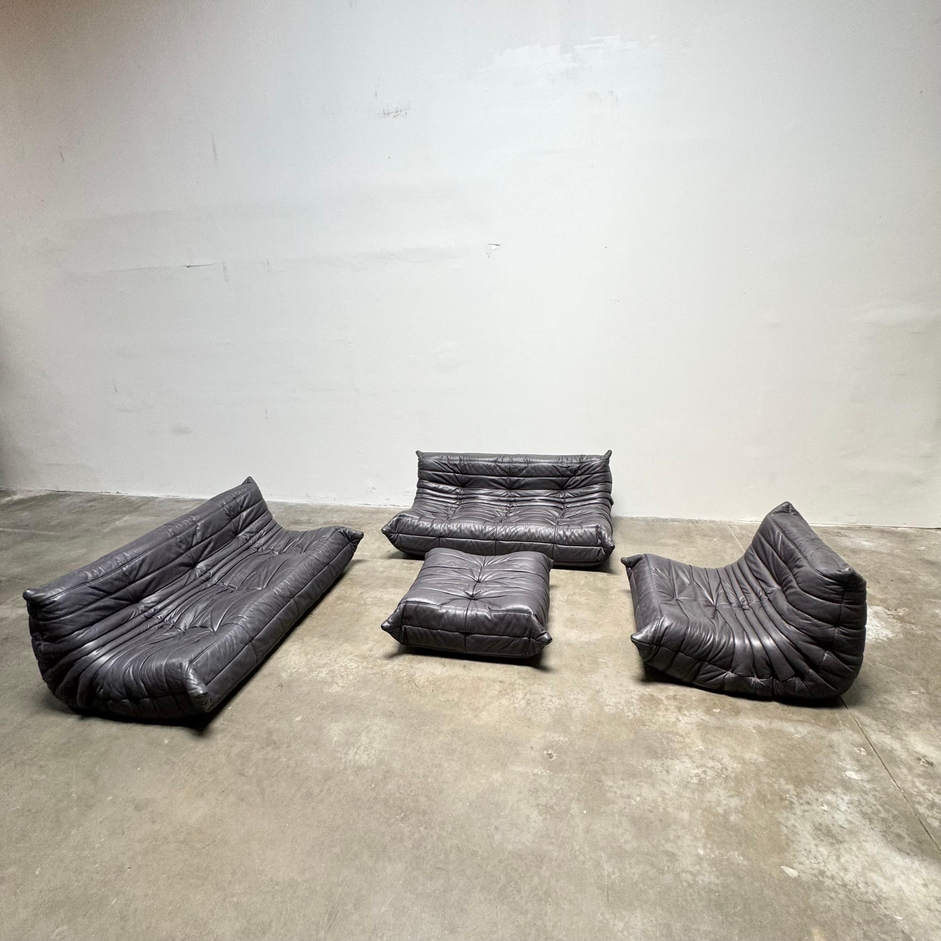 Beautiful authentic 4-piece midnight black leather Togo set designed by Michel Ducaroy for Ligne Roset from the 1980s.

Designer Michel Ducaroy drew inspiration for the Togo's design from an aluminum toothpaste tube noticing it “folded back on