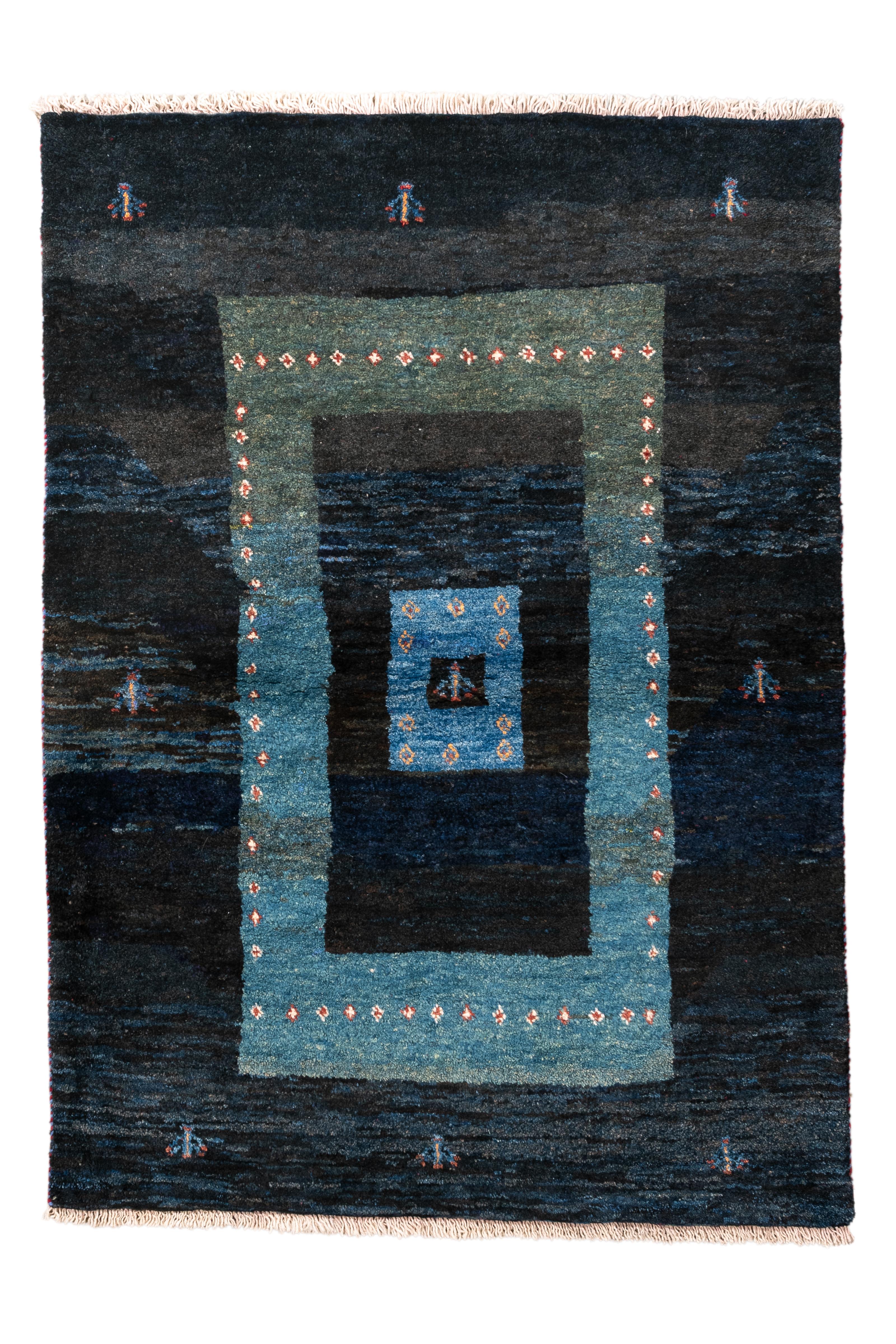  A striking example of tribal minimalism, this handwoven Gabbeh rug features a bold series of nested rectangles in a deep gradient of midnight blues and celadon greens. The central medallion and border are adorned with delicate diamond-shaped motifs