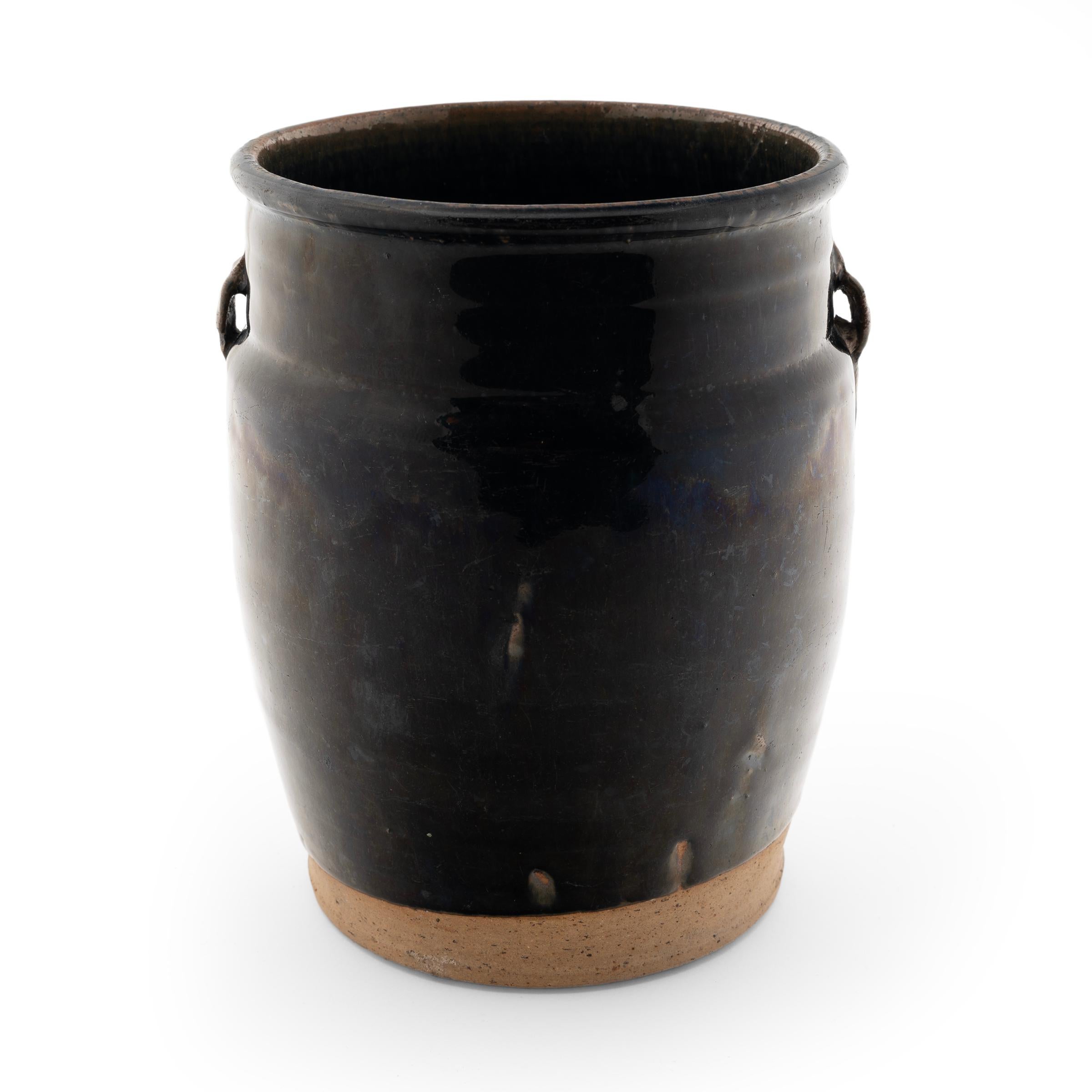 A dark blue-black glaze coats the body of this small kitchen jar, sheeting down the sides and pooling at the sharp angle drawn by its high shoulders. The glazed vessel dates to the early 20th century and was used for storing food and condiments in a