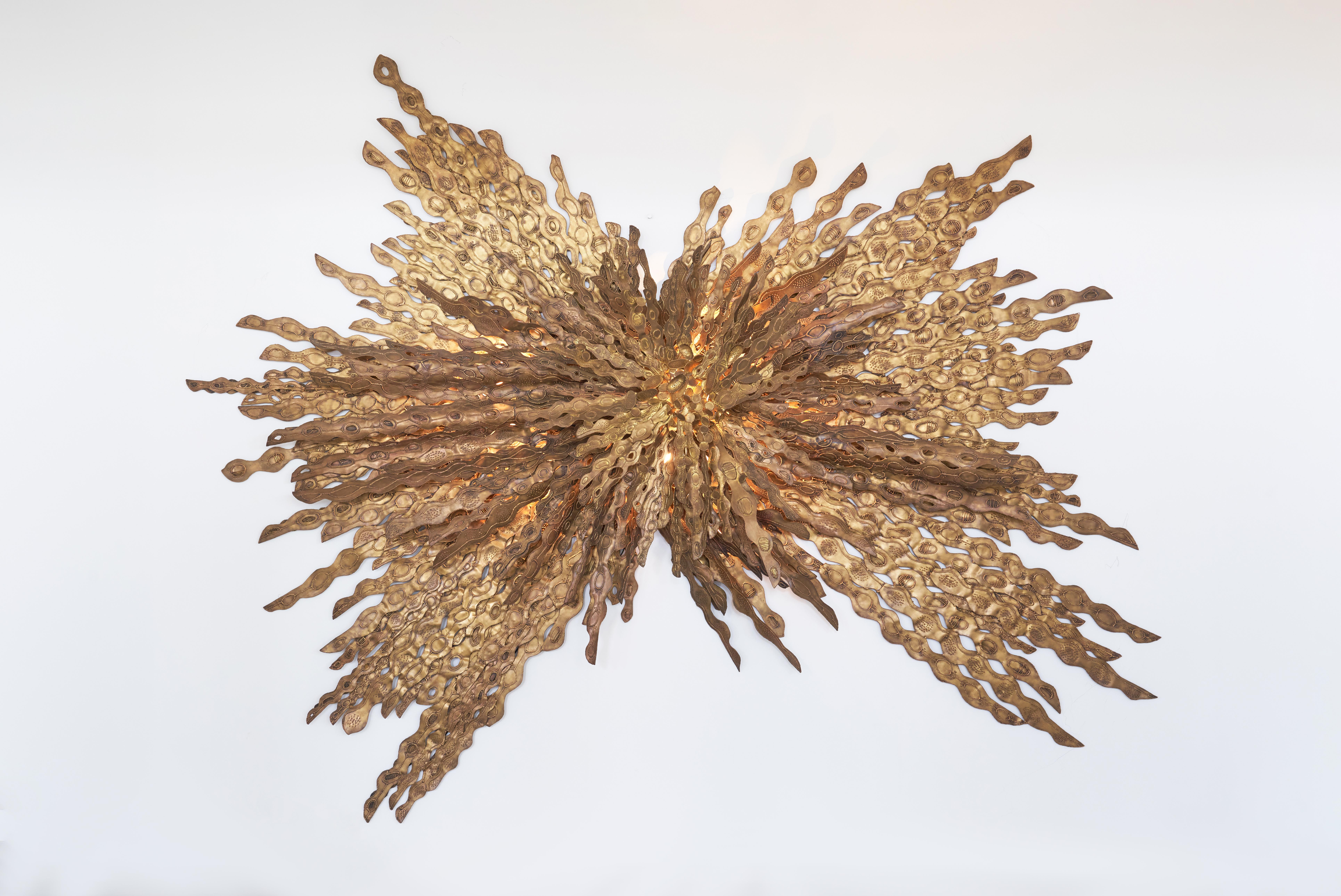 Each piece of metal that comes together to make this patinated-gold sconce is painstakingly cut and welded together through meticulous artisan handcrafting. The careful detailing of each sunray of brass allows for the light to disperse and cast a