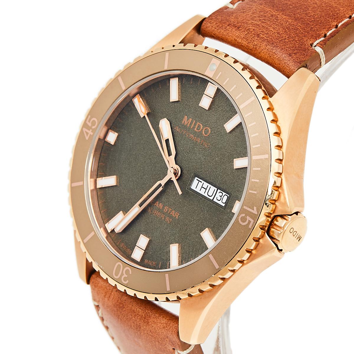 This luxe Mido Automatic watch features a green dial with elegant hour markers, three hands, and a day-date window. The 42.5 MM case in rose gold PVD stainless steel is held by brown leather straps. The water resistance of up to 200 meters is an