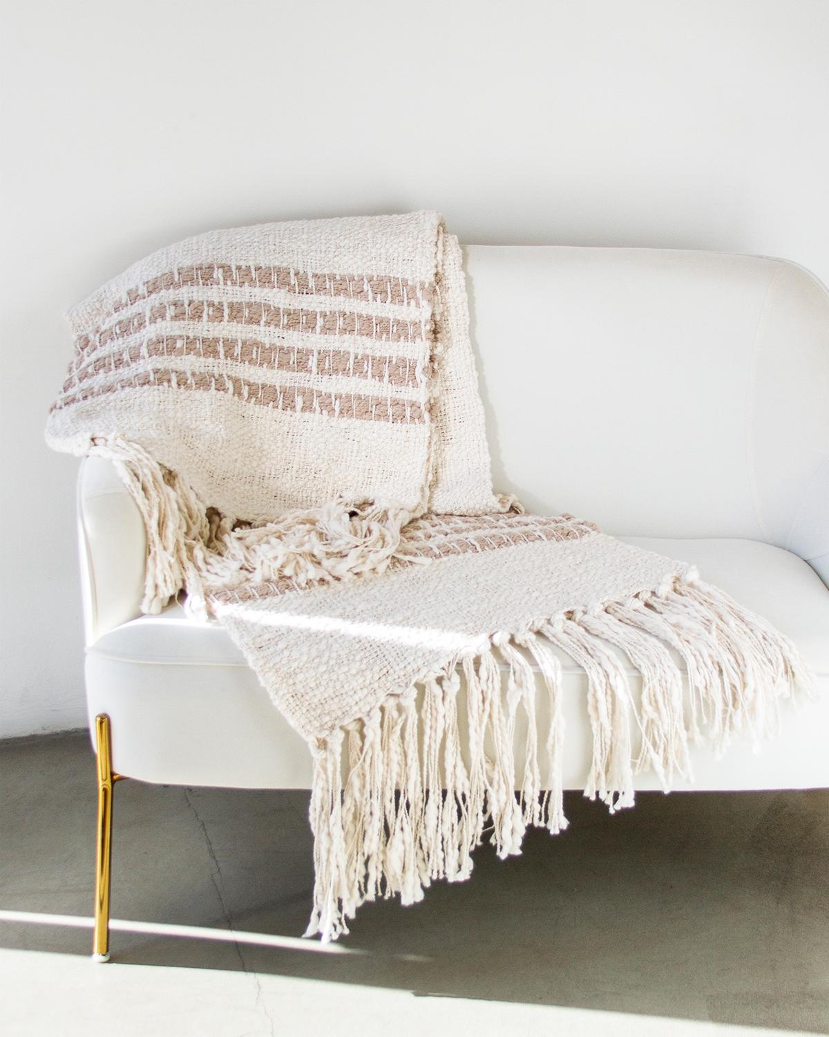 Elevate your home decor with the sophisticated and rustic Miel Ivory Cotton Throw Blanket. Crafted with a soft boucle cotton weave and adorned with stripe detailing, this blanket adds a touch of quiet luxury to any space. The open weave weft and