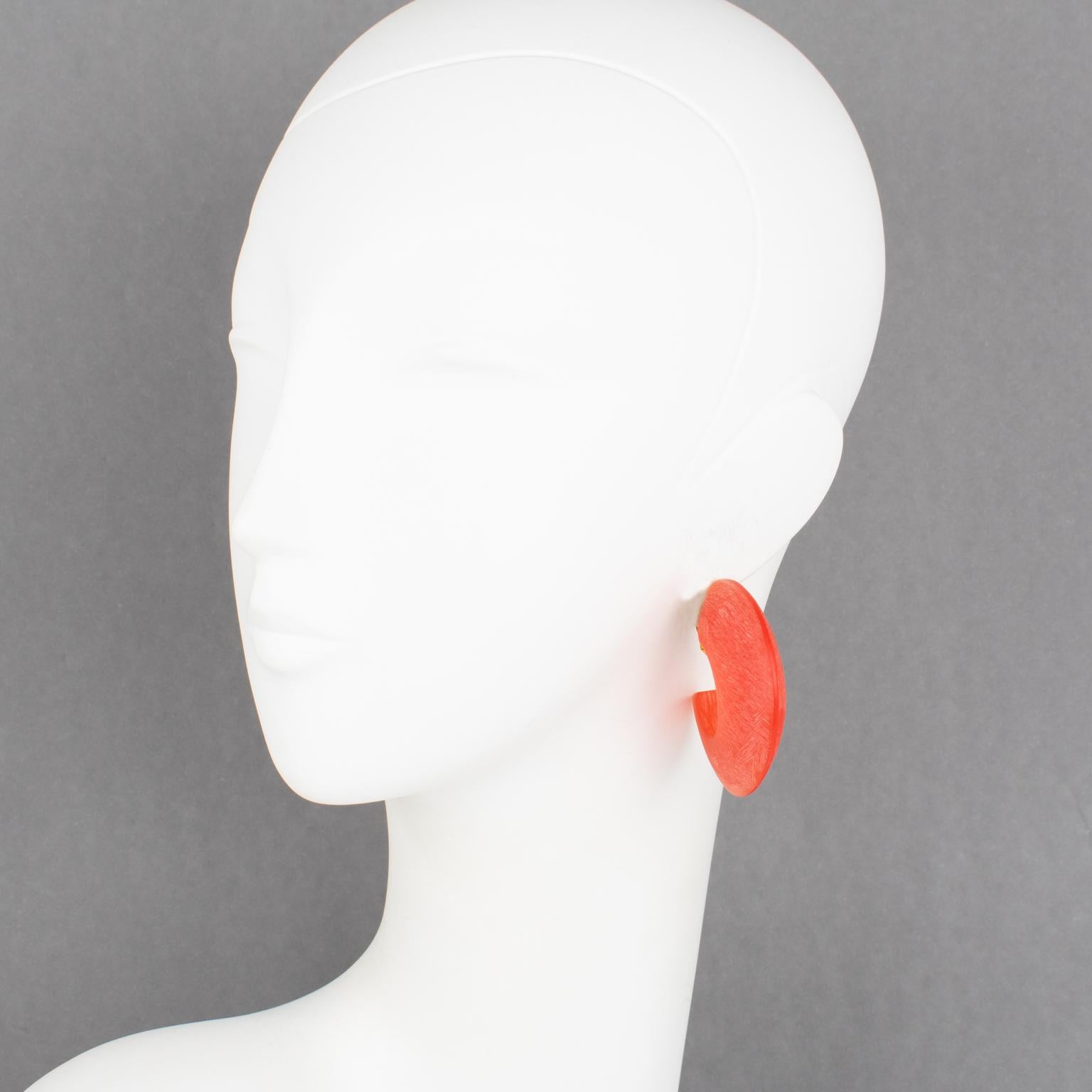 These beautiful hand-crafted modernist plexiglass or resin clip-on earrings were created by Marie Therese and Christian Migeon, known as Migeon & Migeon. The rare massive carved loop shape has a dazzling, delicious orange watermelon hue and is