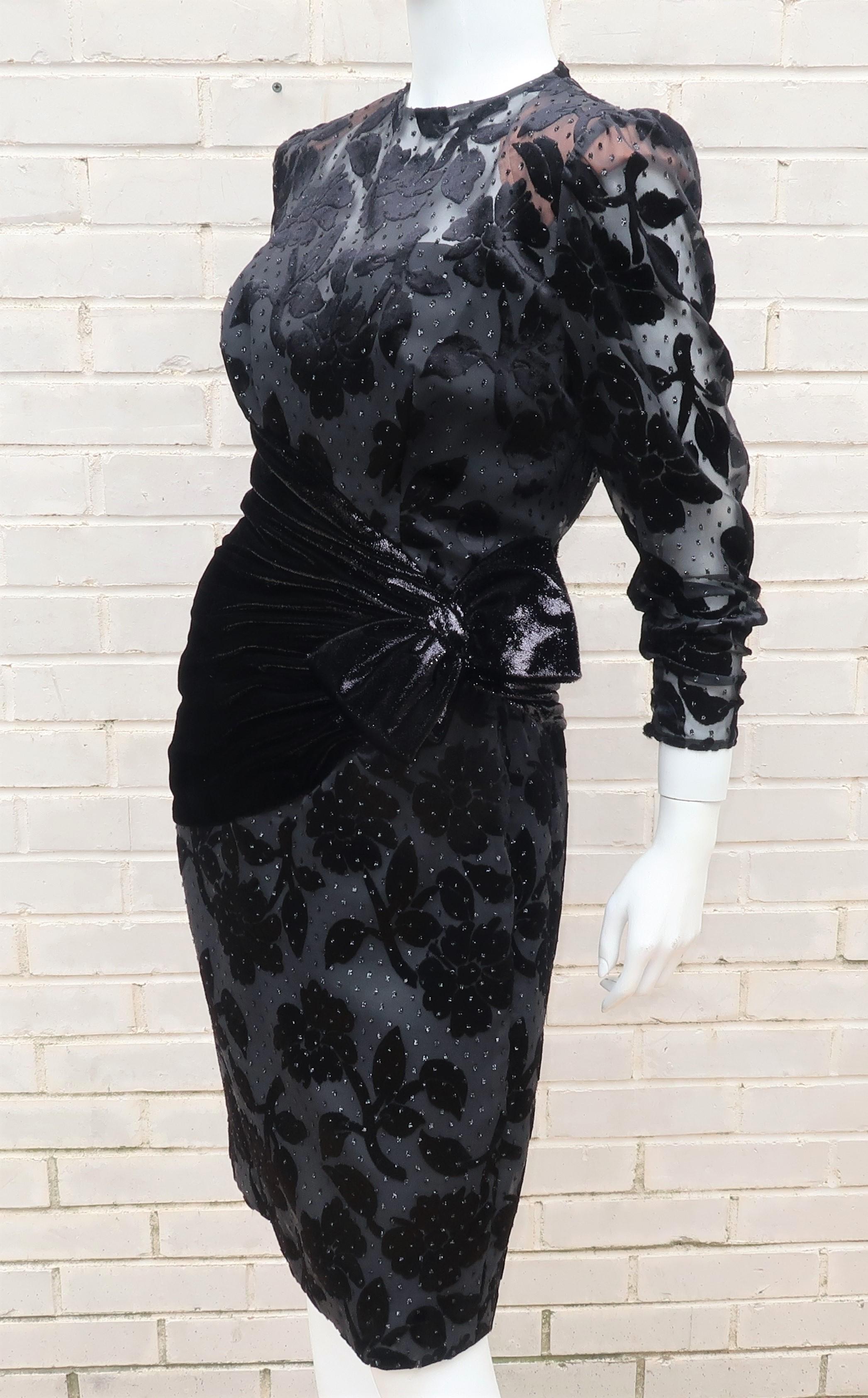 A black cocktail dress by Anne Marie Gabalis for Mignon in a classic 1980's silhouette including strong shoulders and an emphasized waist.  This elegant look is modernized by the combination of a cut velvet in a floral pattern accented by glitter