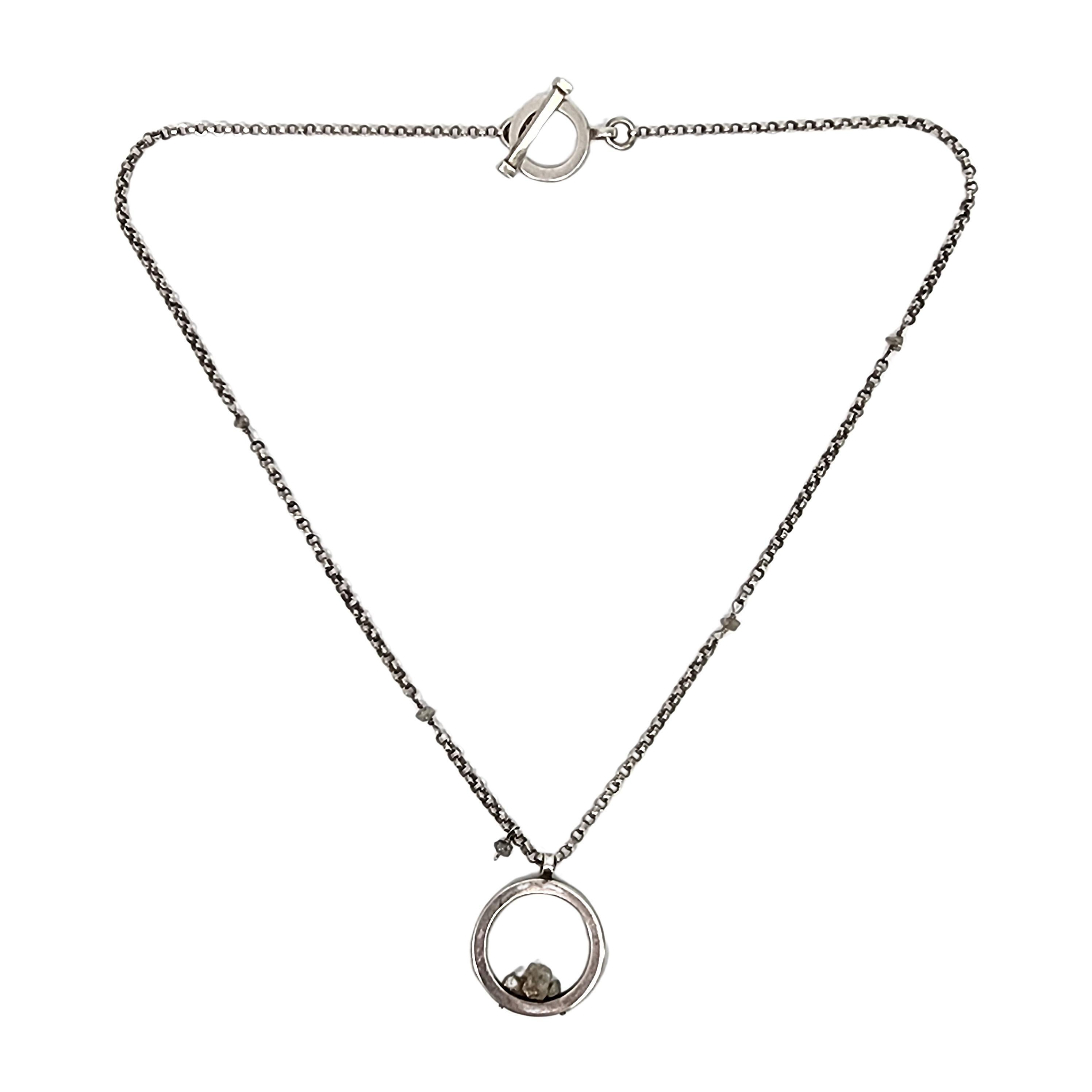 Sterling silver circle with small stones necklace and earring set by Mignon Faget.

The necklace features an open circle pendant with small stones that are green/yellow in color, the chain features the same stones in a grey color interspersed on the