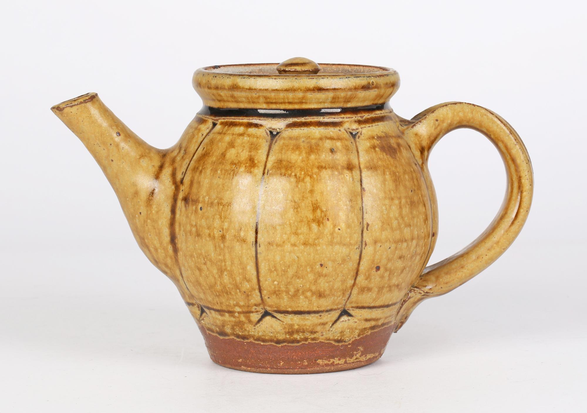 A stylish English studio pottery teapot and cover decorated in brown ash glazes by renowned potter Mike Dodd (English, b. 1943) and dating from the 20th century. The teapot of rounded form has incised panelling around the body with a large loop
