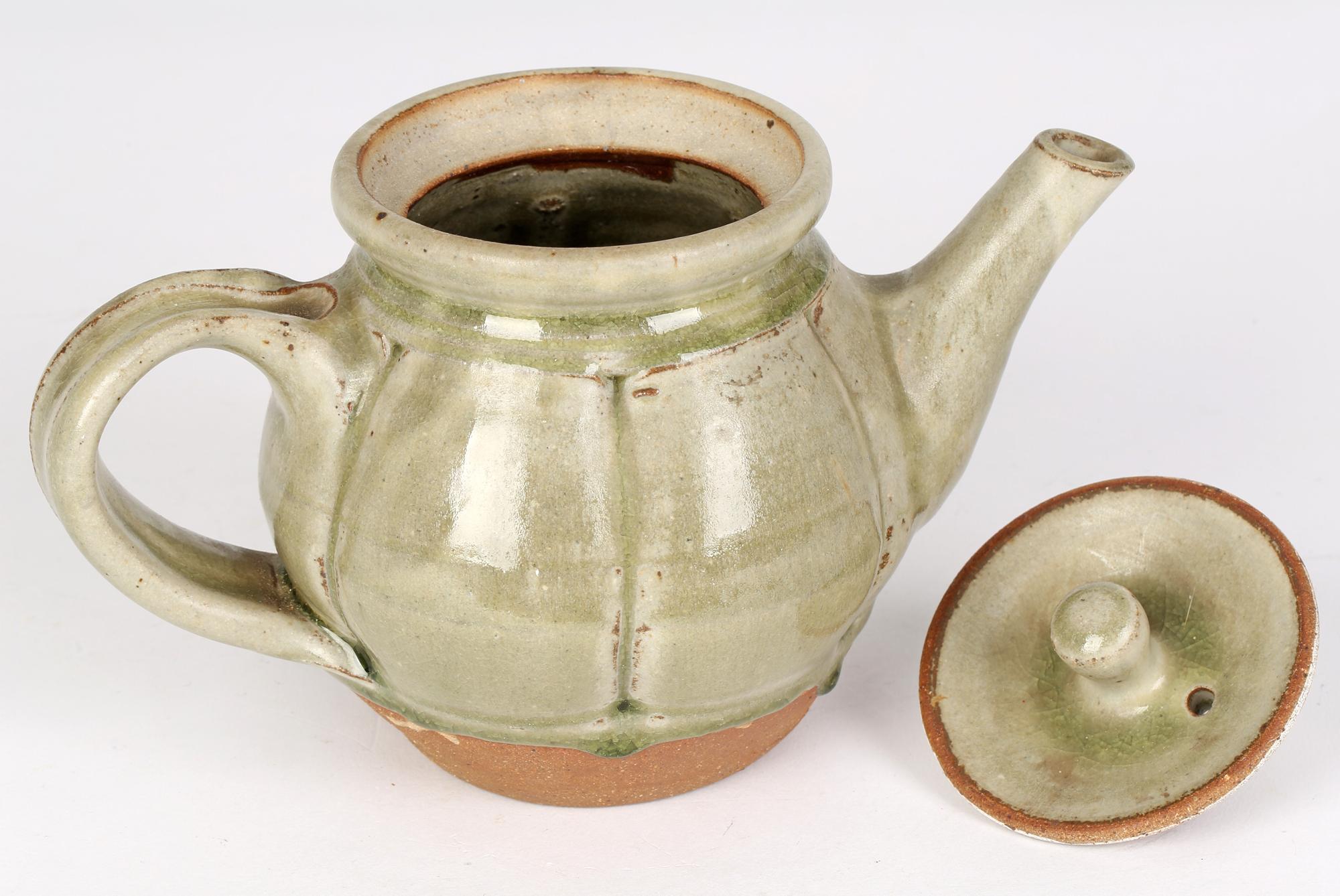 A stylish English studio pottery teapot and cover decorated in green ash glazes by renowned potter Mike Dodd (British, b. 1943) and dating from the 20th century. The teapot of rounded form has incised paneling around the body with a large loop