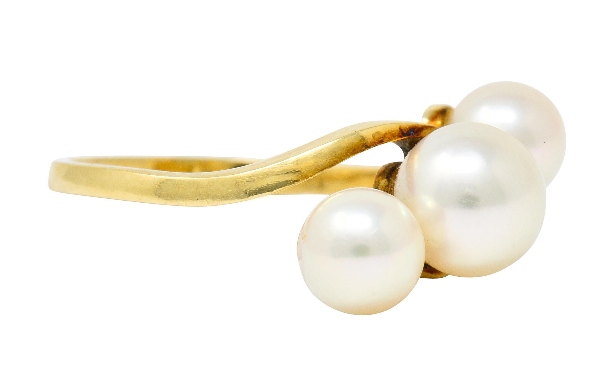 Delicate bypass style ring with polished gold shoulders as a wave-like design

Centering three round cultured pearls, well-matched cream body color with slight rosè overtones and excellent luster

Larger center measures approximately 6.9 mm, while